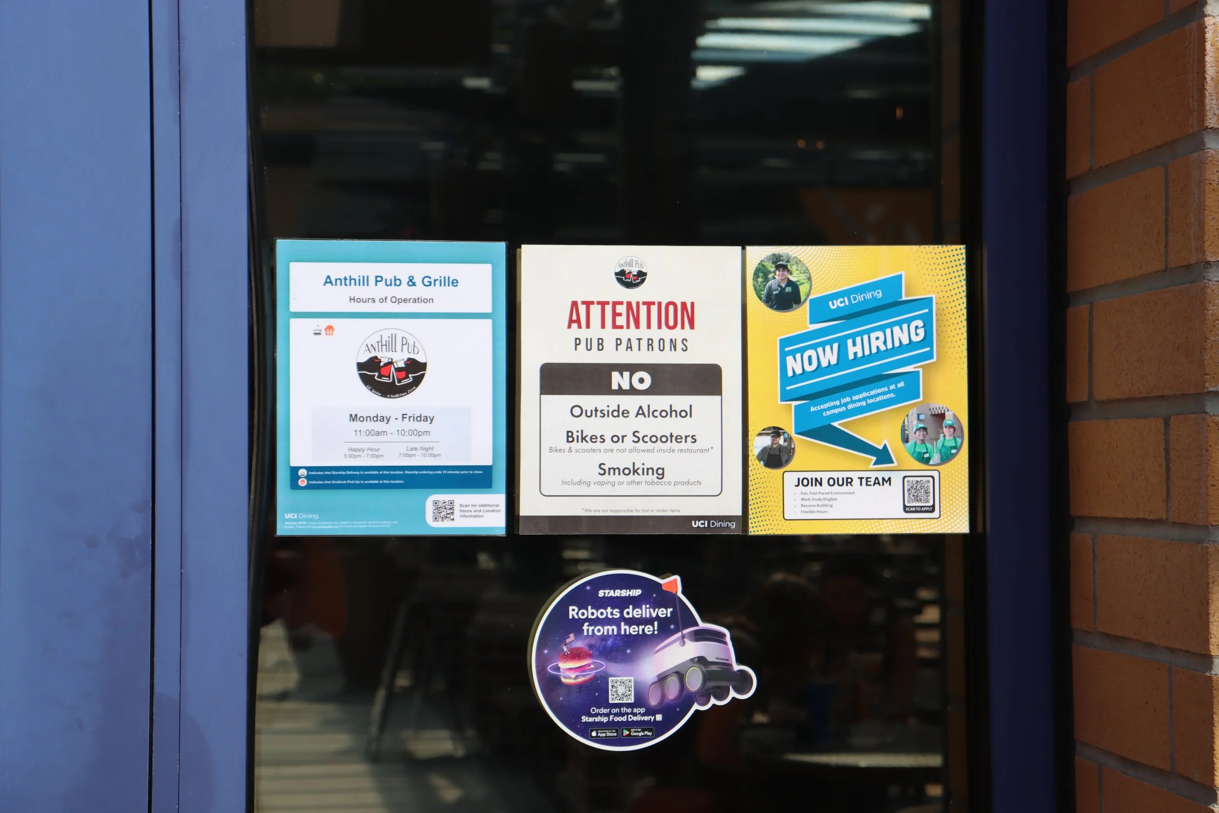 Signage on a window for Anthill Pub & Grille, stating hours of operation Monday through Friday from 11:00 am to 10:00 pm, with happy hour from 5:00 pm to 7:00 pm and late night from 7:00 pm to 10:00 pm; a notice prohibiting outside alcohol, bikes, sk