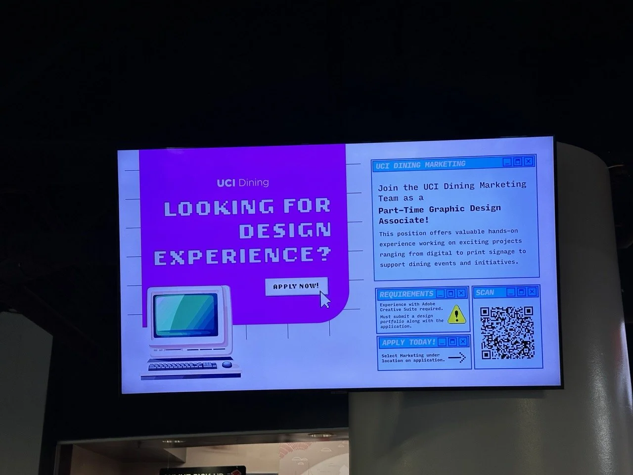Digital recruitment advertisement on a screen for a part-time graphic design position at UCI Dining, with a purple background, pixelated text, a computer image, and a QR code.
