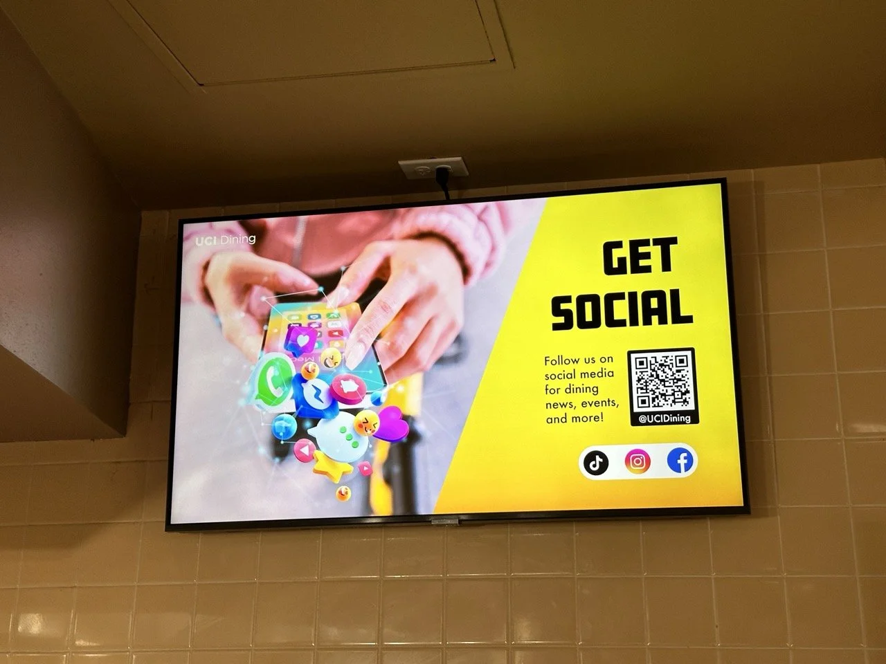 Digital advertisement encouraging social media engagement for UCI Dining, featuring a hand holding a smartphone with colorful social media icons, alongside the text "Get Social" and a QR code.