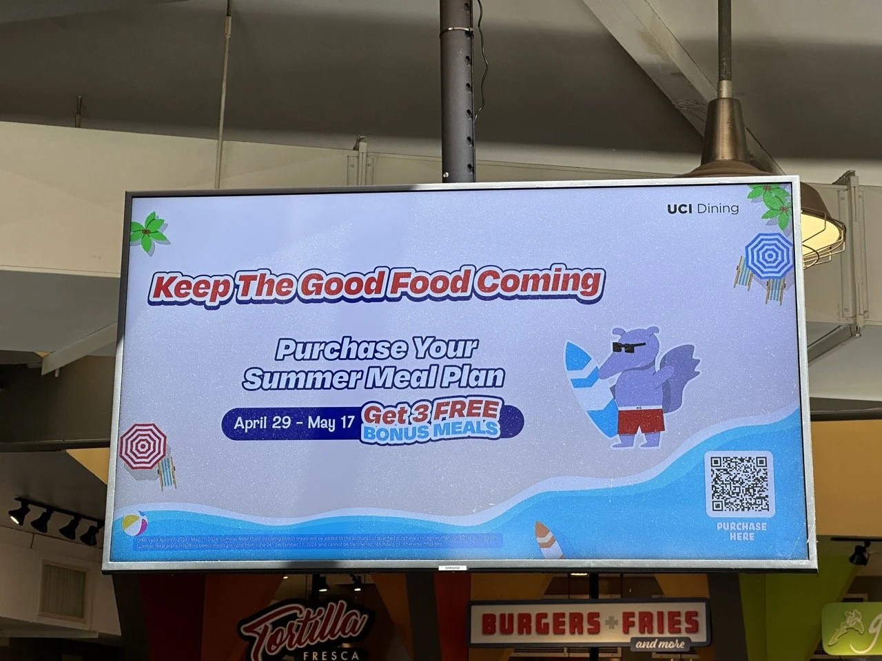 Digital sign promoting a summer meal plan with a special offer of 3 free bonus meals, running from April 29 to May 17, with a QR code for purchase, in a dining area.