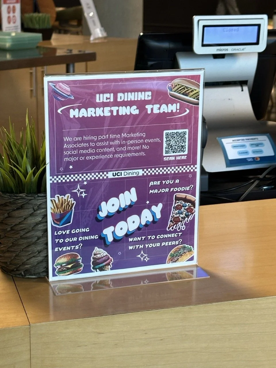 Promotion sign on a restaurant counter encouraging people to join the UCI Dining Marketing Team, with images of fast food items and a QR code.