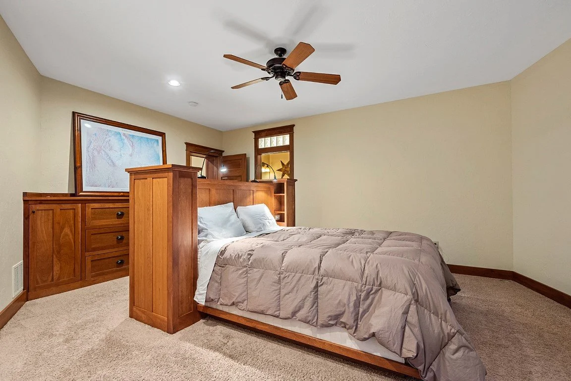 Lodging for our all inclusive Wyoming guided waterfowl hunt with a bedroom with a wooden bed frame, beige walls, ceiling fan, and built-in dark wood shelves at the head of the bed.