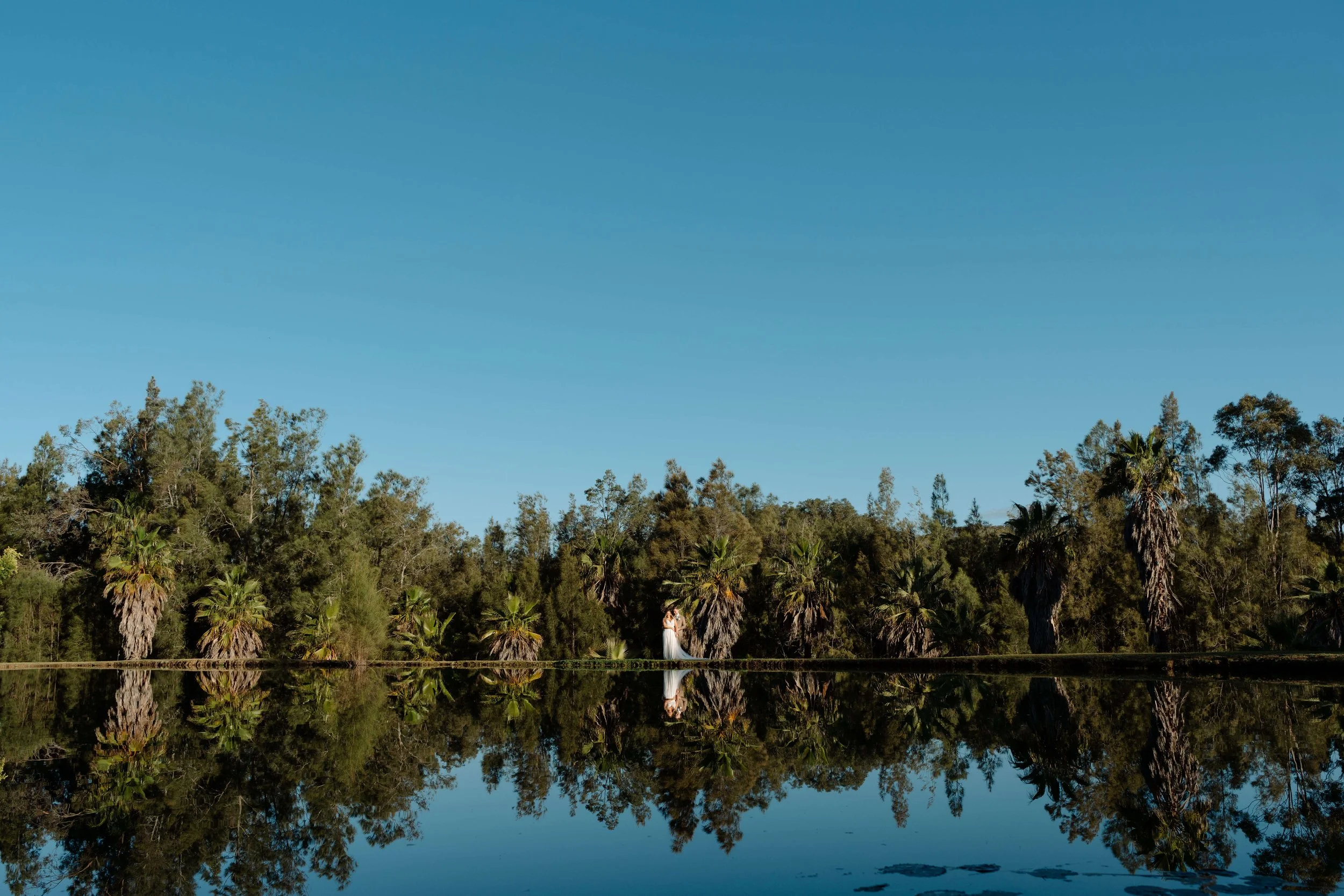 Bride and groom embracing beside the lagoon at Leaves & Fishes