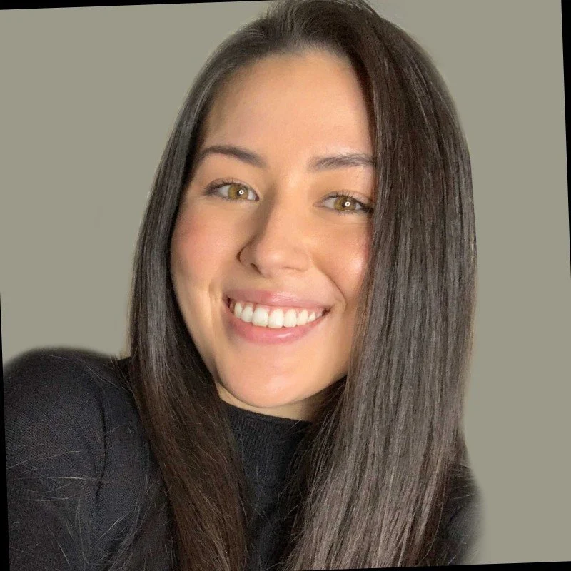 Smiling person with long black hair wearing a black shirt, neutral background.