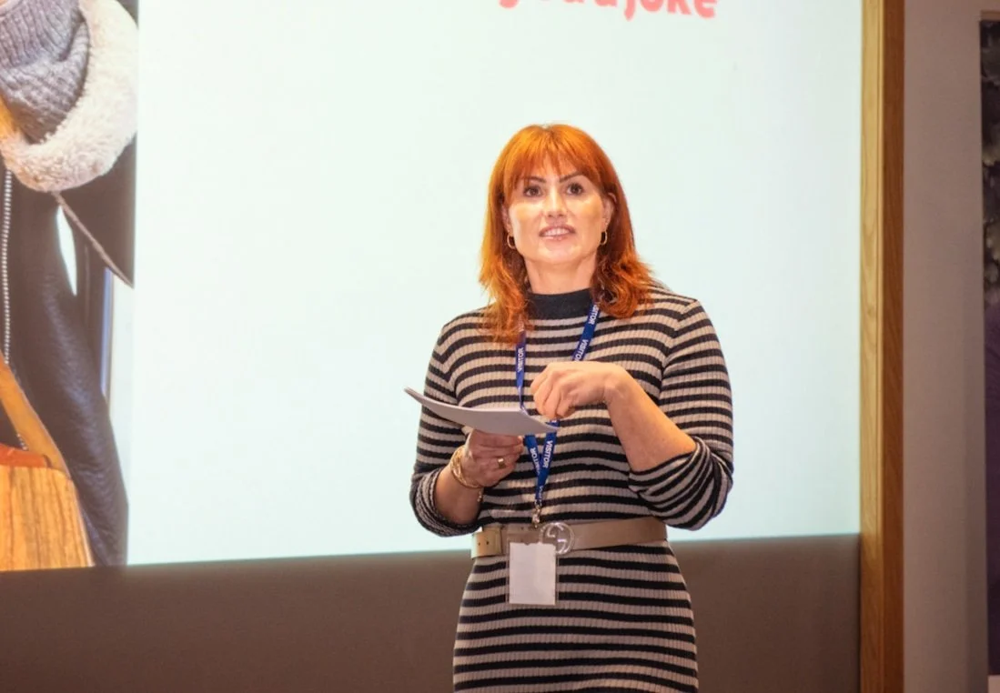 Red haired woman in striped dress holding cue cards presenting on stage