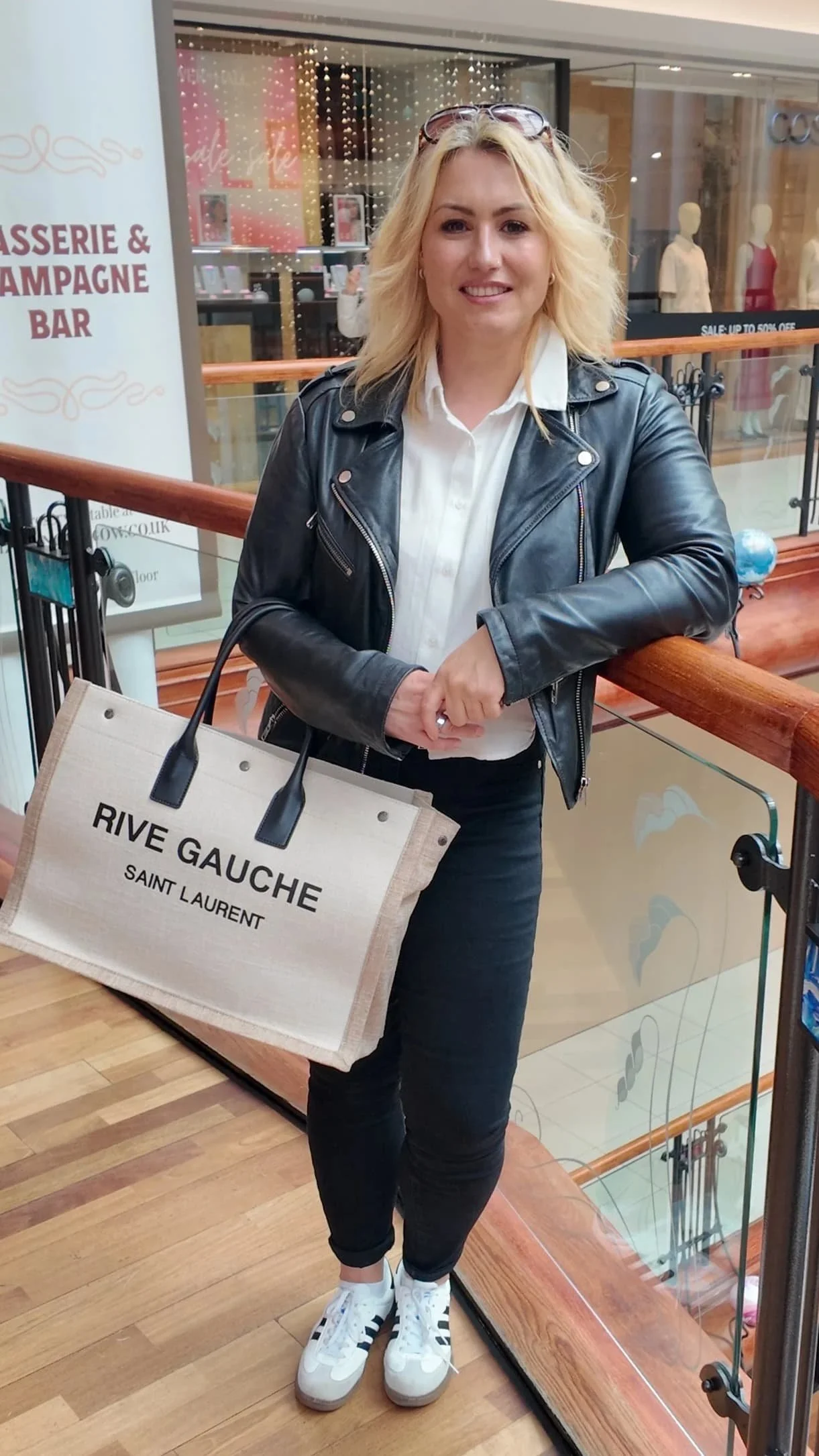 blonde woman holding rive gauche bag on a balcony
