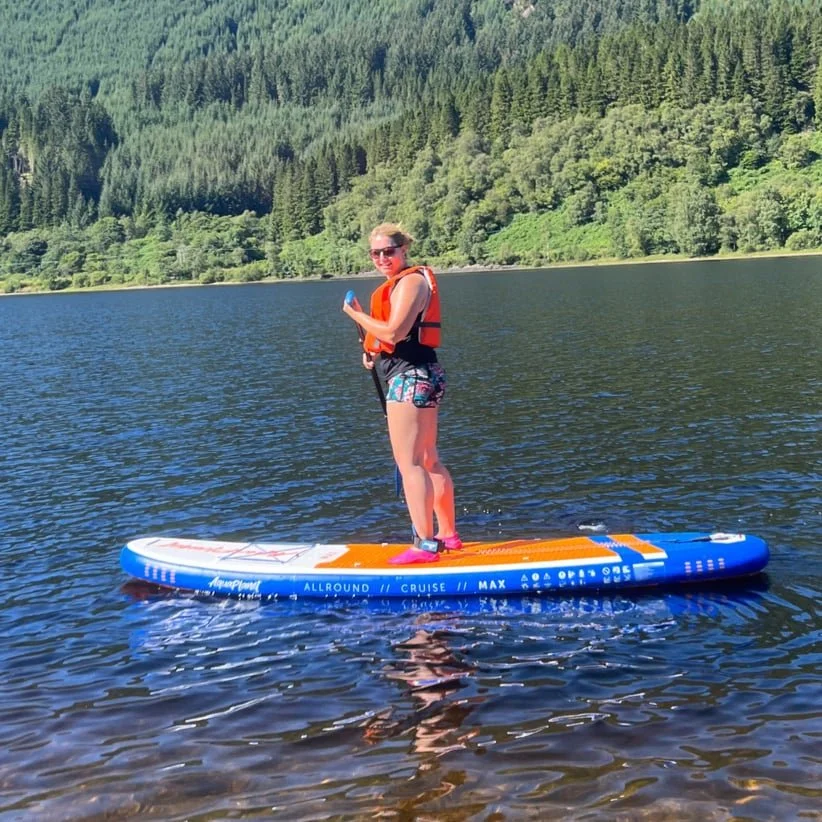 white woman standing on orange and blue paddleboard with paddle in hand