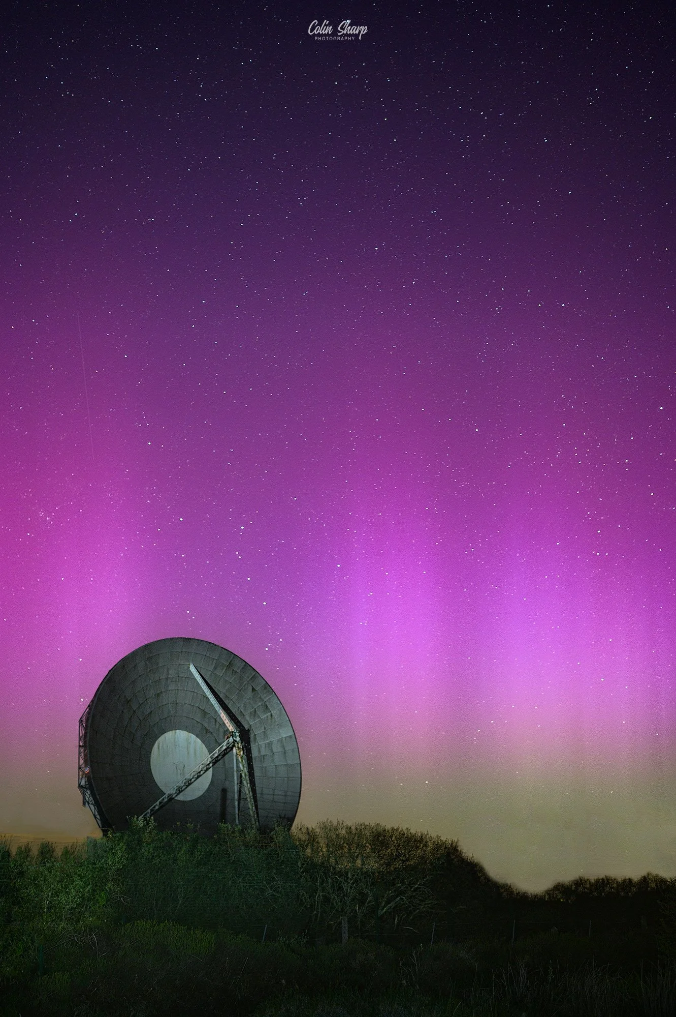 Night sky filled with stars and the aurora borealis, featuring a large radio telescope dish, known as Arthur, in the foreground at Goonhilly Earth Station