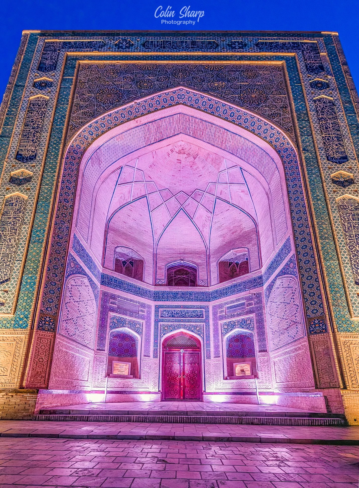 A blue hour photograph of the entrance to the Kalon Mosque lit by artificial coloured lighting.