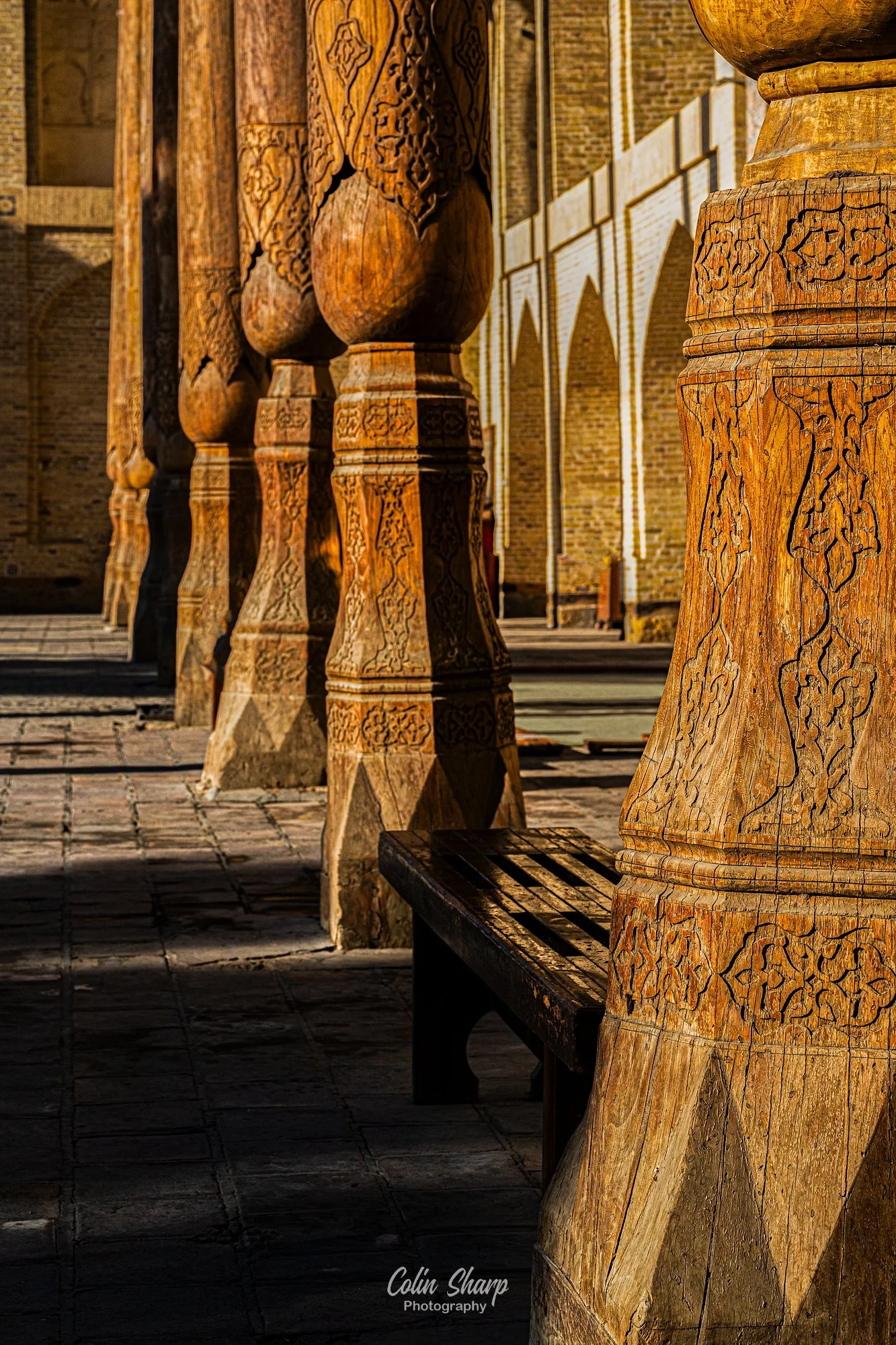 An image showing the painted and craved wooden pillars of the Bolo-Hauz Mosque in the glow of the golden hour sunshine.