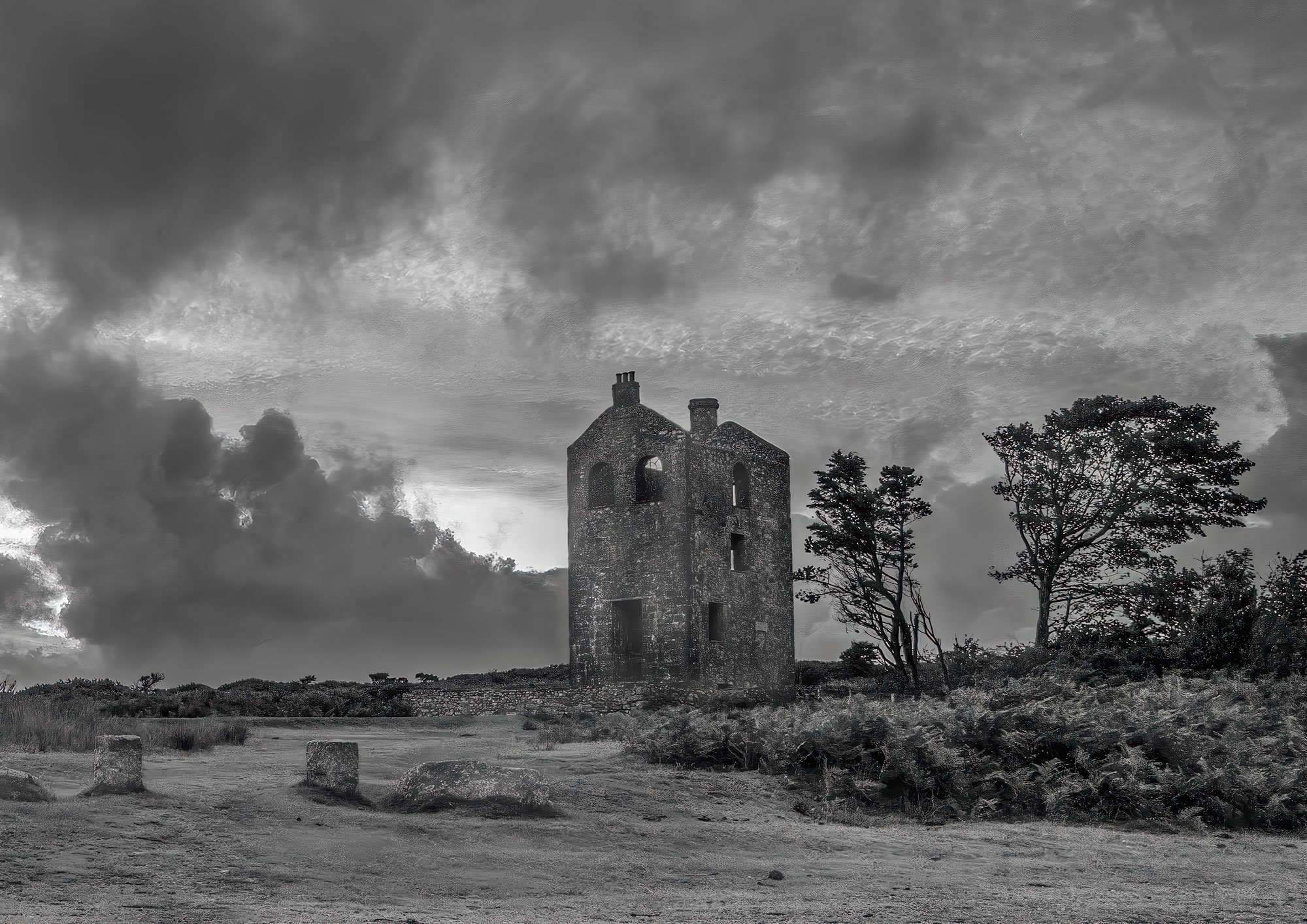 Black and white landscape of old mine ruins at South Phoenix Mine taken at sunset near Minions on Bodmin Moor with stormy sky and wind blown trees and moorland vegetation