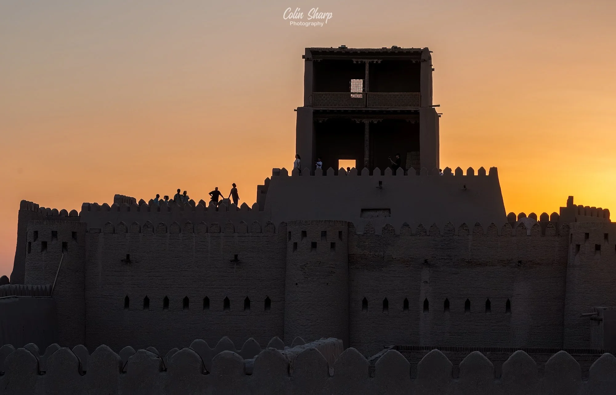 A photo of the silhouette of the Khuna Ark with people on the parapets as the sun was setting behind them