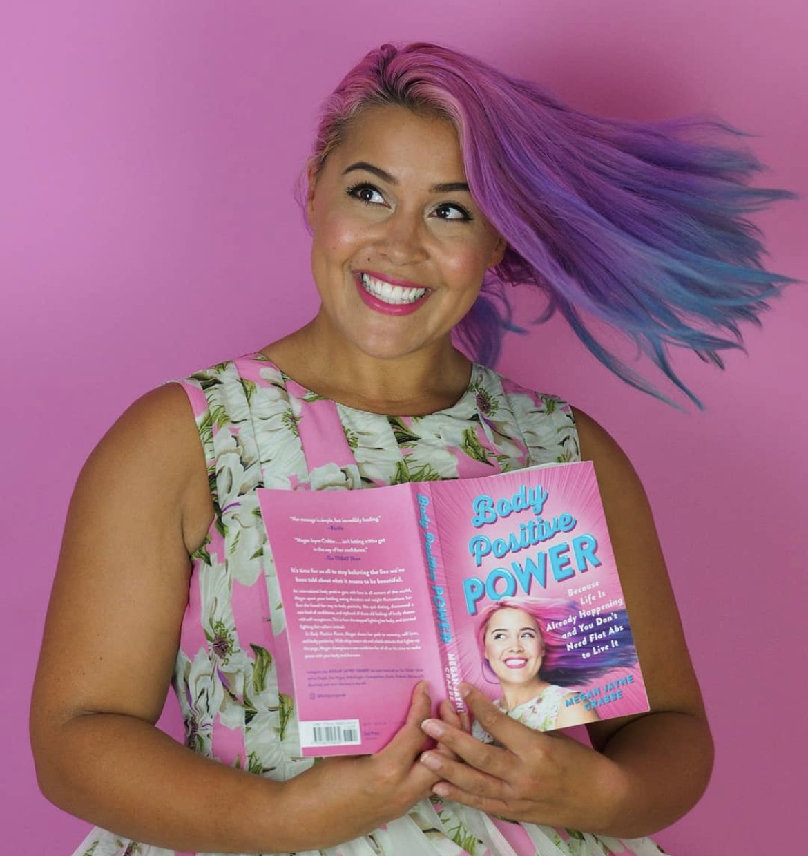  Megan Jayne Crabbe (Bodyposipanda) with purple and blue hair holding a copy of the US edition of her book, Body Positive Power. 