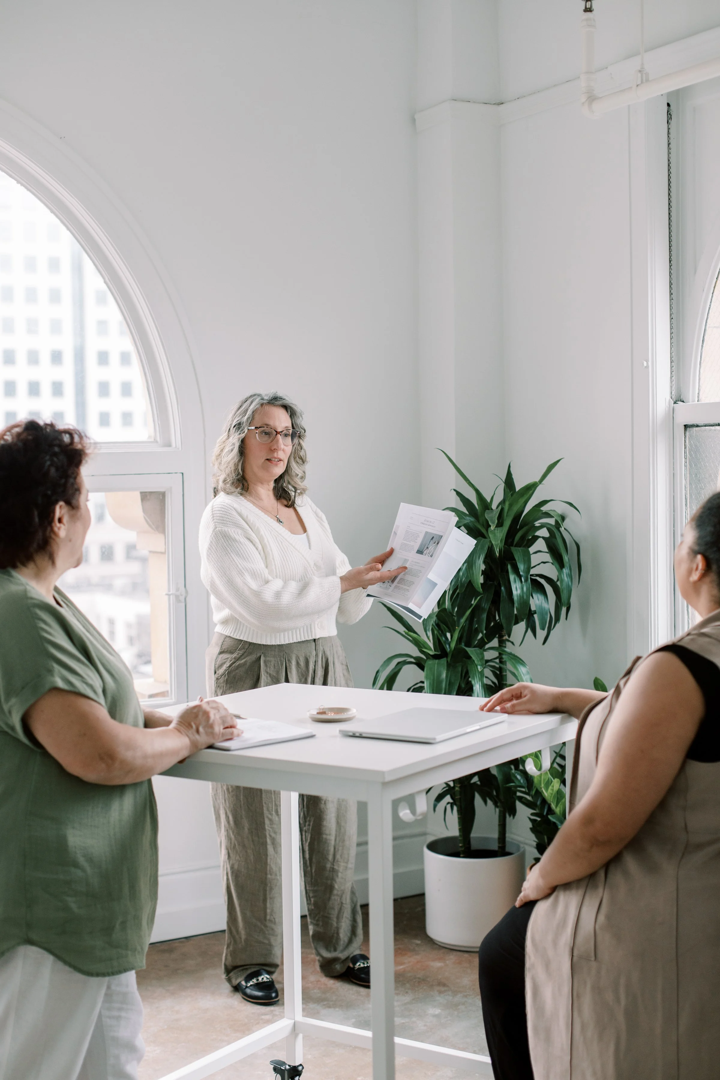 three women gathered around a standing desk reviewing and talking about business documents