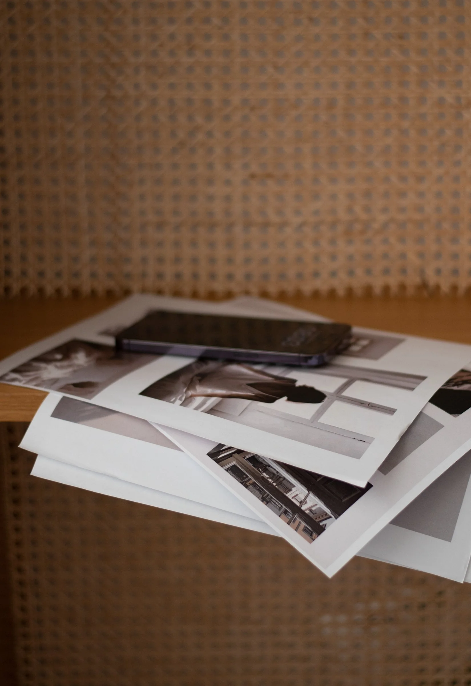 Warm light highlights a textured chair piled with printed photos and a smartphone, evoking a quiet creative moment in a cozy interior.