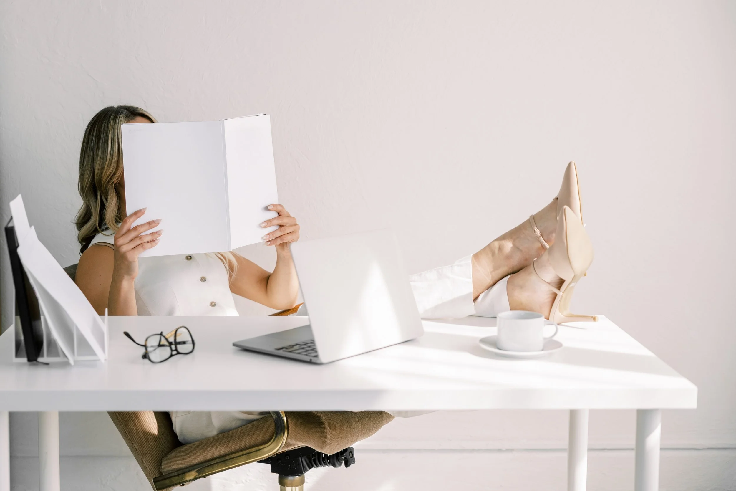 Woman dressed in white sitting at a desk with her feet up while she reviews documents in a folder