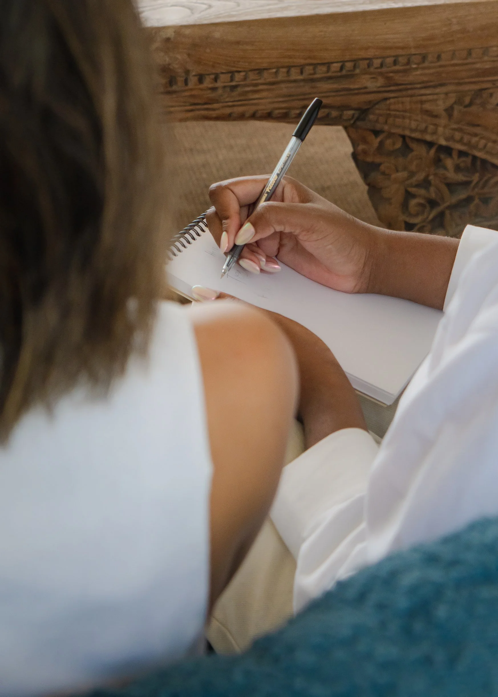 Over-the-shoulder view of a woman writing in a notebook, emphasizing focus and mindful planning in a relaxed setting.