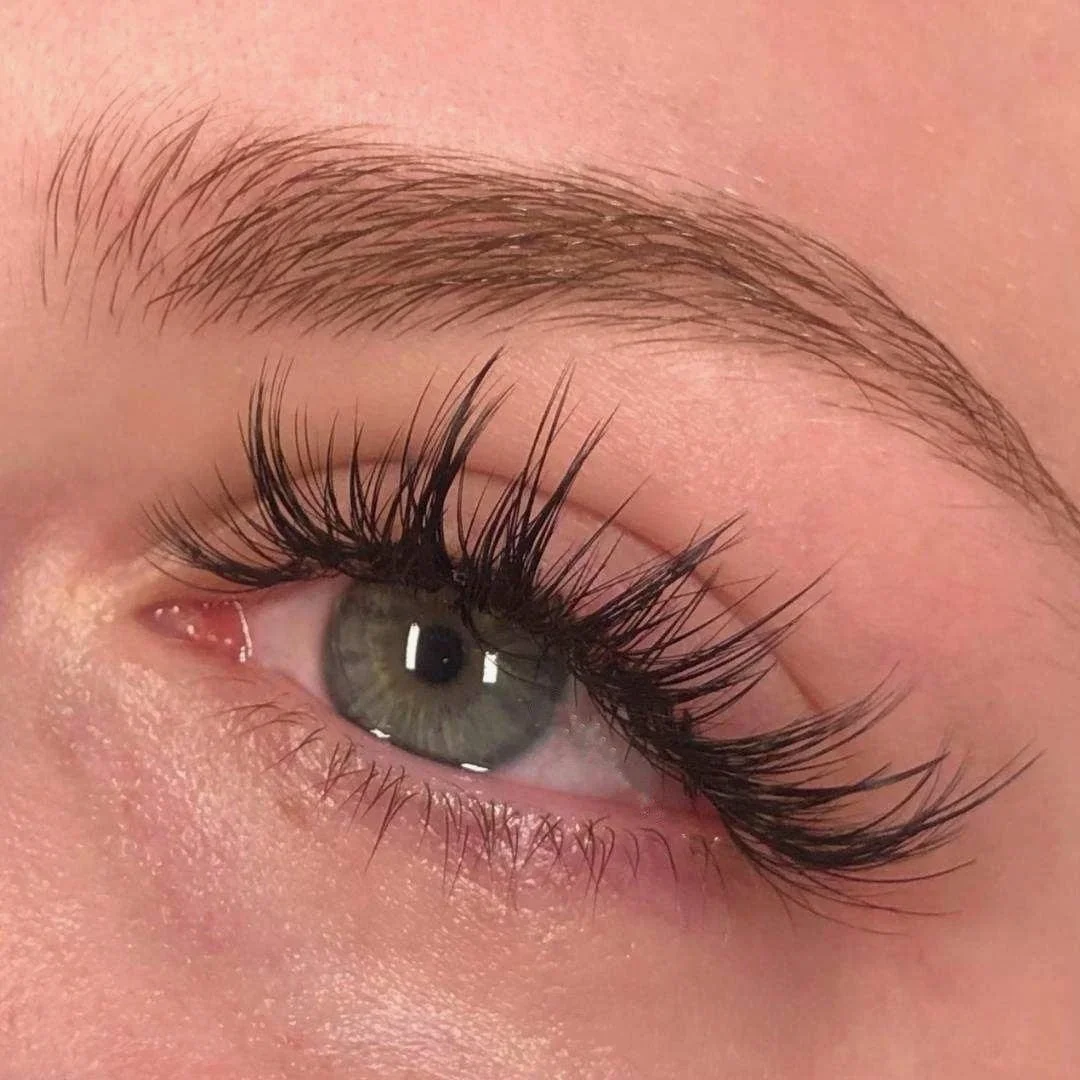 Close-up of a human eye with light blue-green iris, long curled eyelashes, and well-groomed eyebrow.