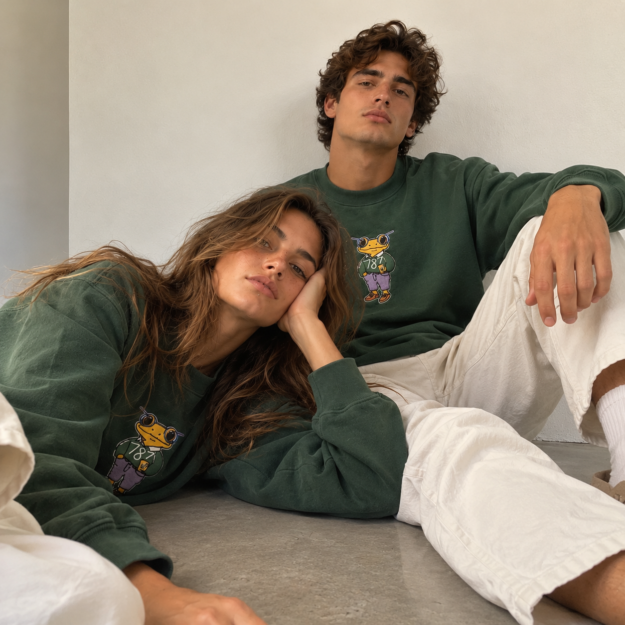 Two people wearing matching Mr. Coquí forest green embroidered crewneck sweatshirts by 787 Coffee with cream pants, unisex relaxed fit