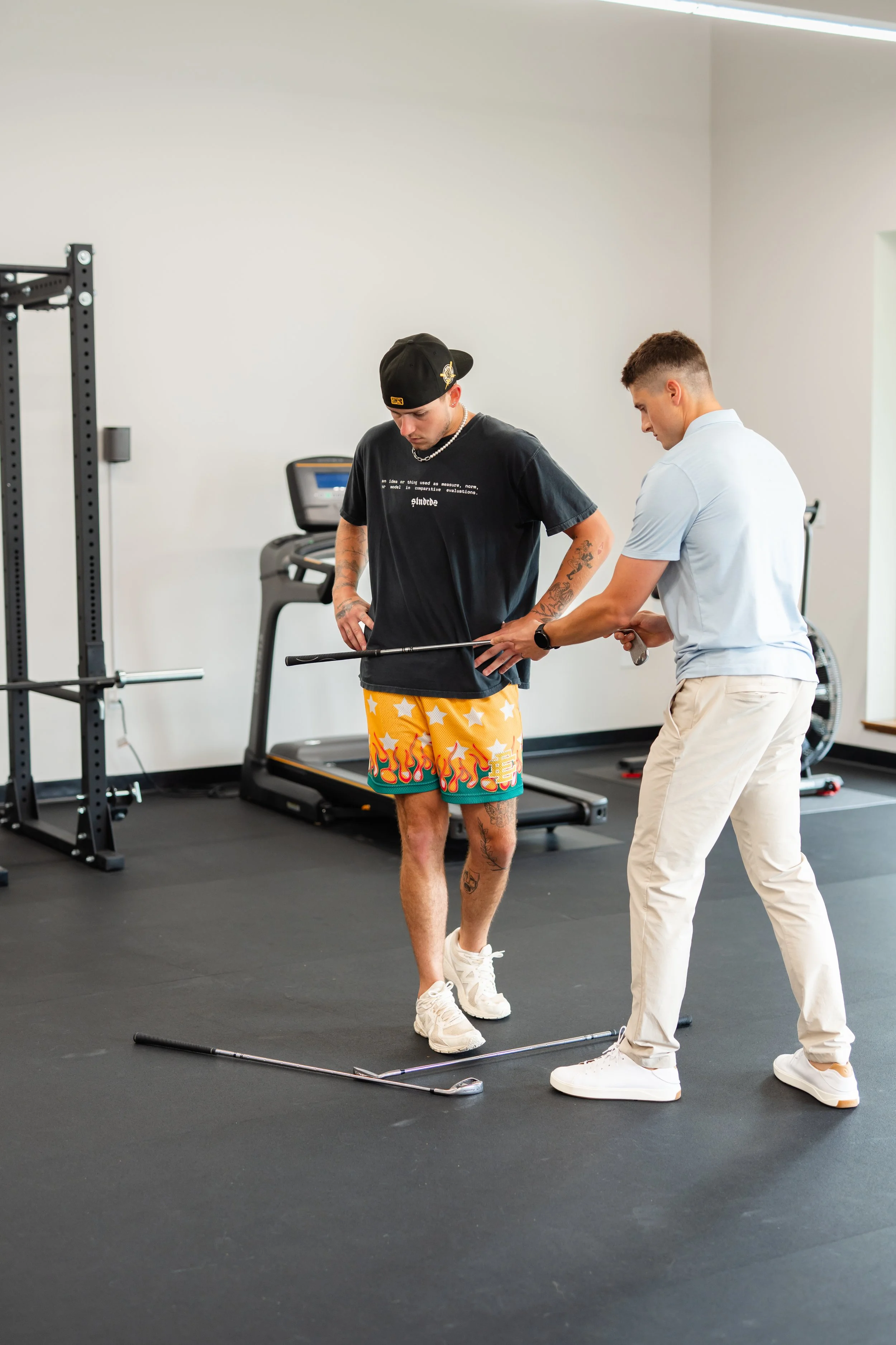 A fitness trainer helping a man on a golf simulator in a gym.