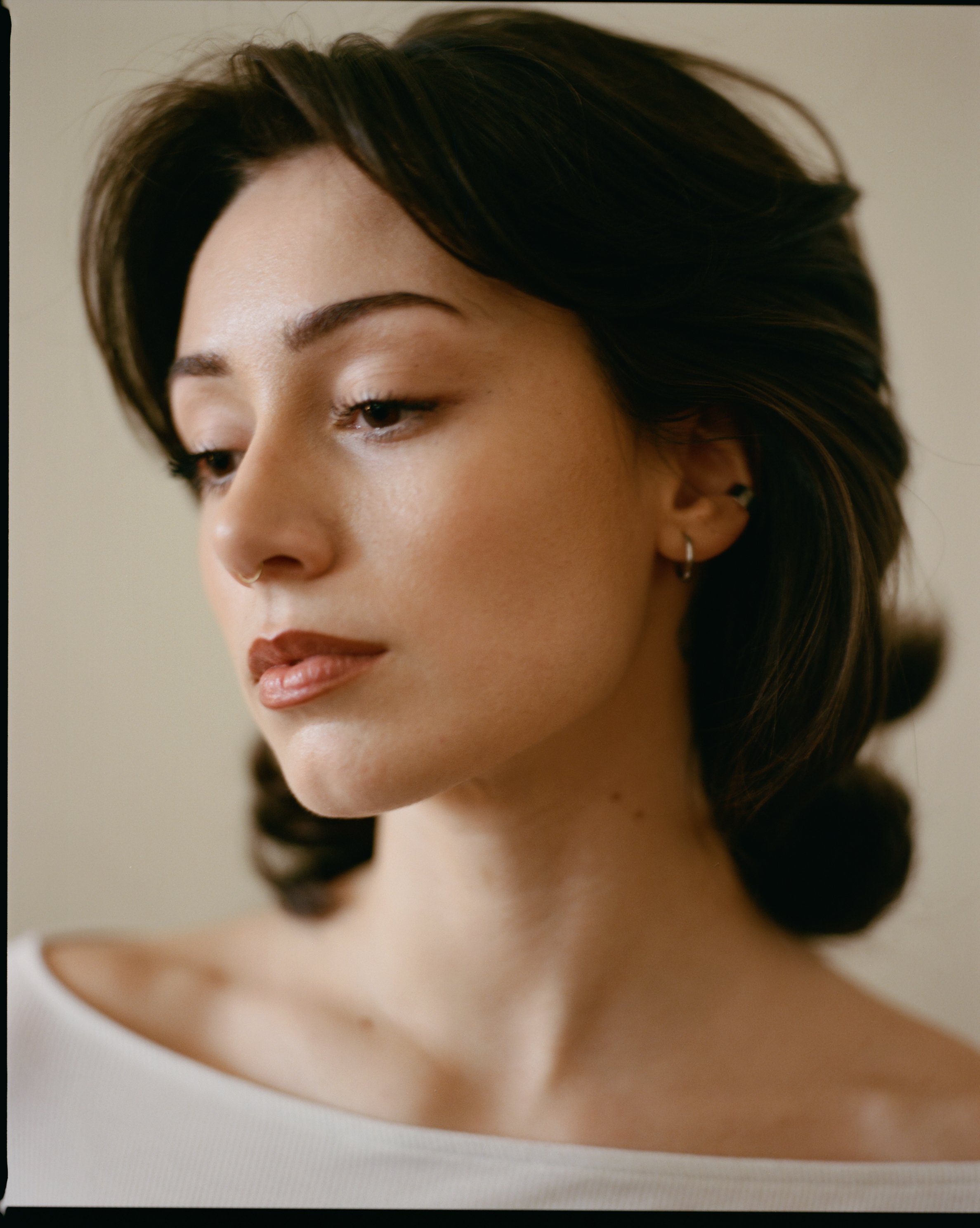 Close-up of a woman's face with short dark hair, earrings, and makeup, looking down.