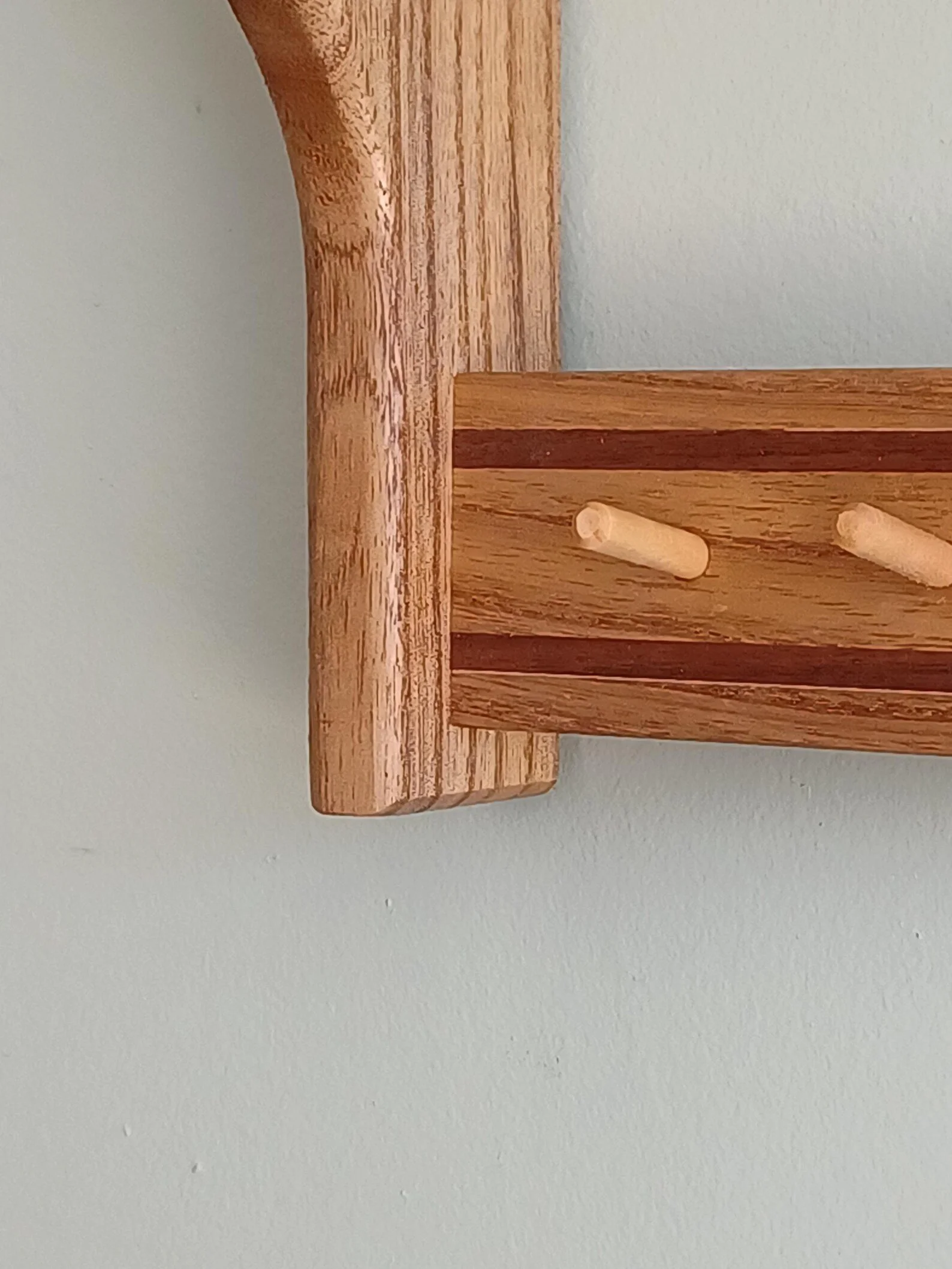 Close-up of a wooden rack or furniture with two small peg-like wooden supports, against a white wall background.