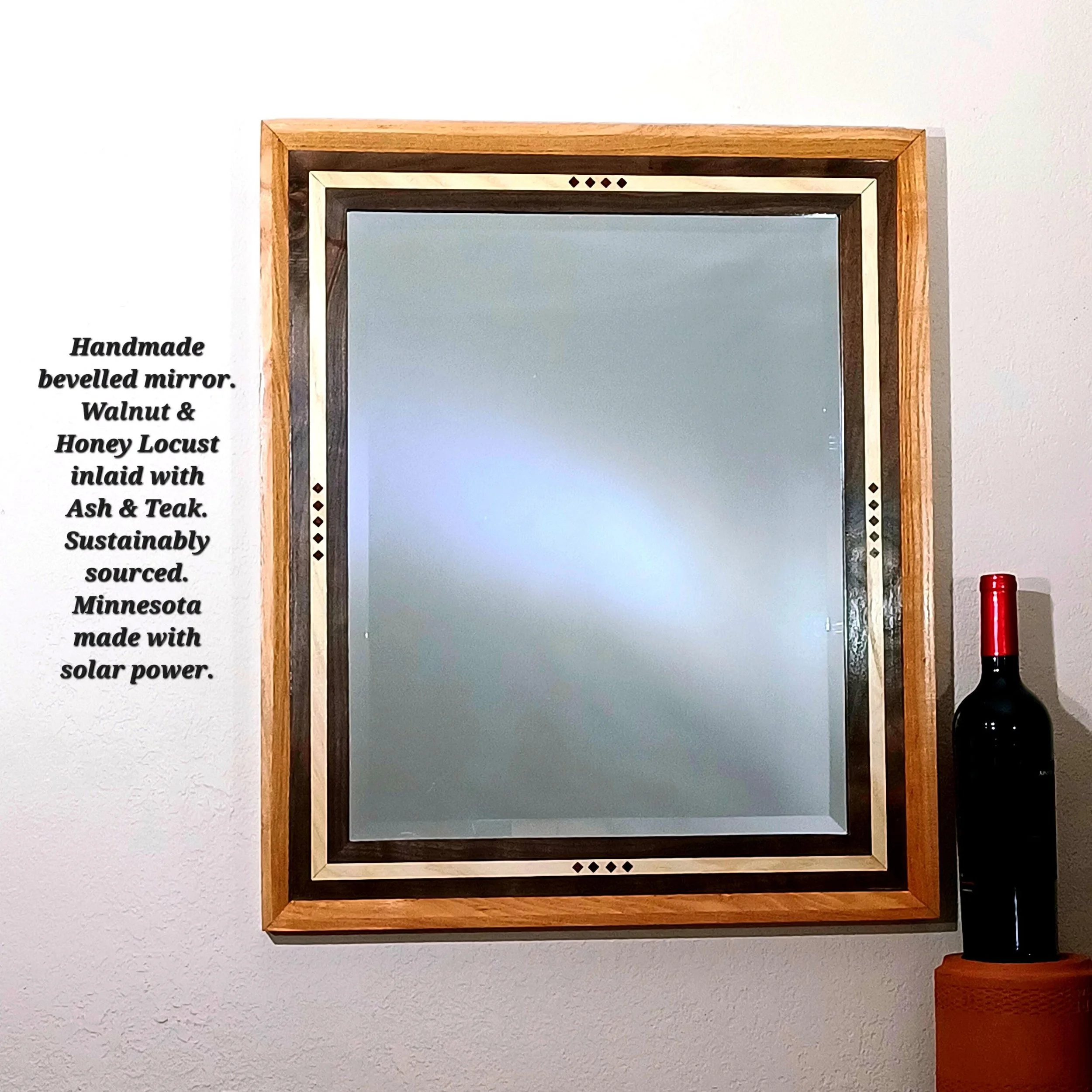 A handcrafted Walnut and Honey Locust frame, including a bevelled mirror and inlaid with Ash and Teak, mounted on a white wall.
