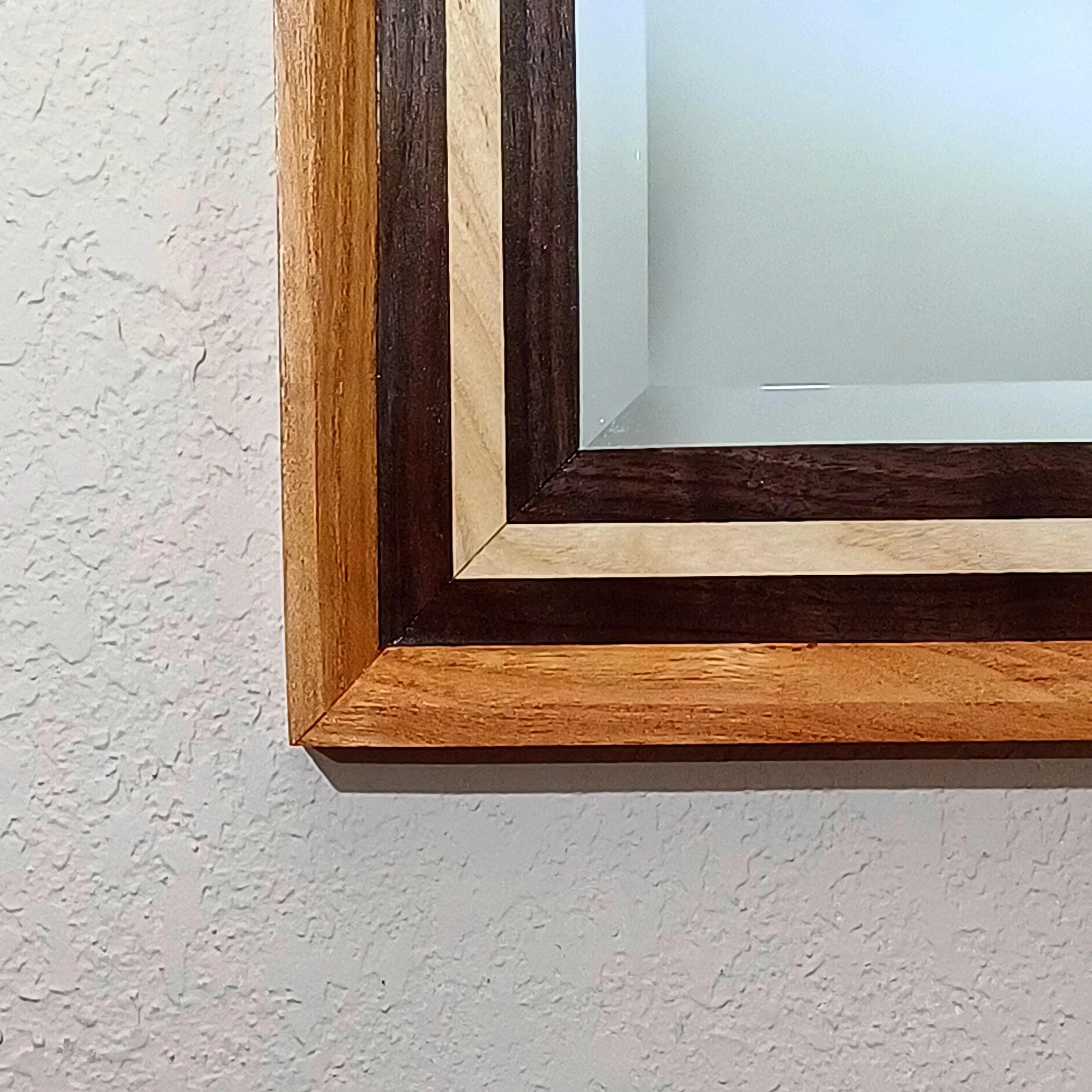 Close-up of a decorative wooden frame holding a beveled mirror, with a textured white wall in the background.