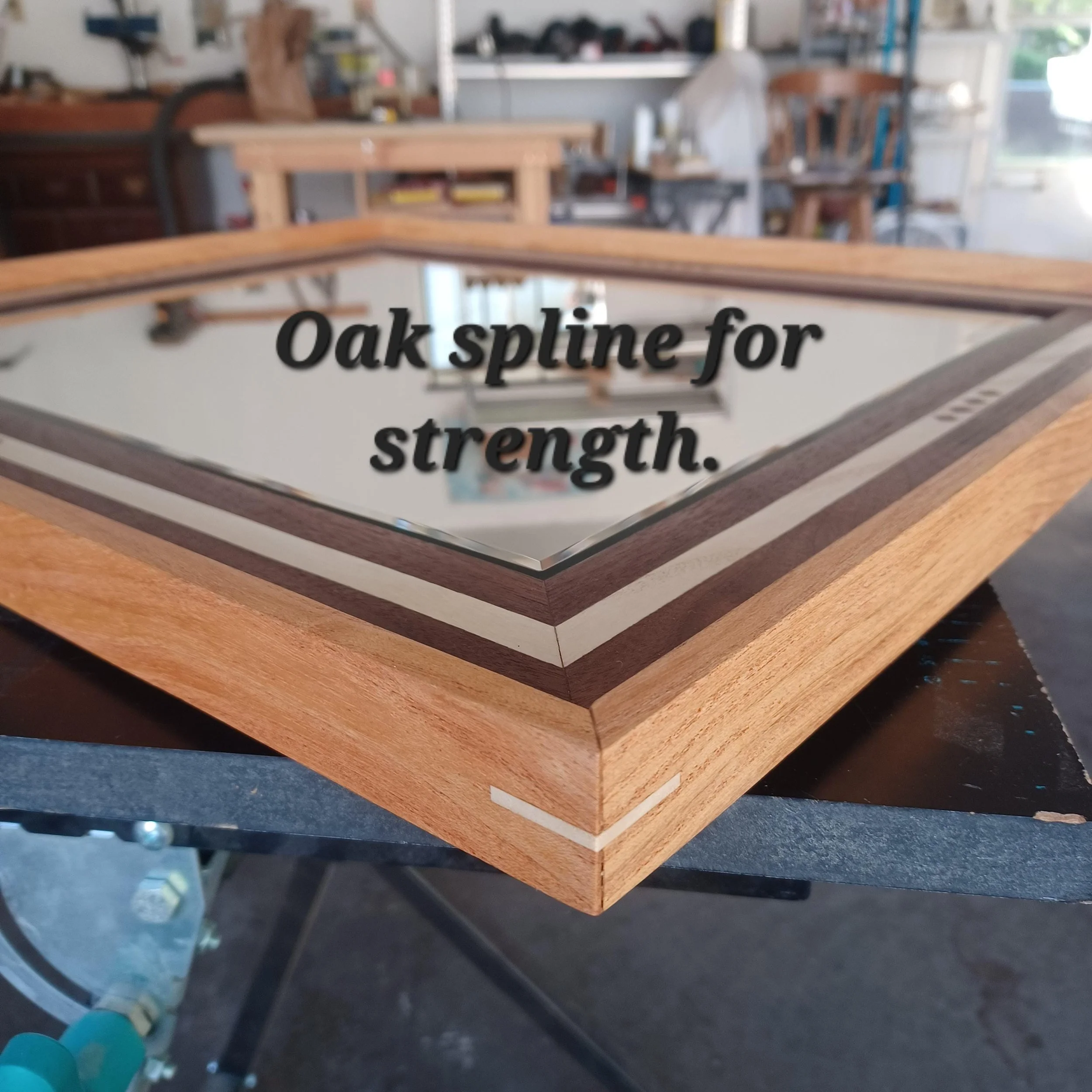 A workshop with various tools and woodworking equipment, a mirror with text 'Oak spline for countertops' visible on it, and a workbench. The background shows shelves with supplies.