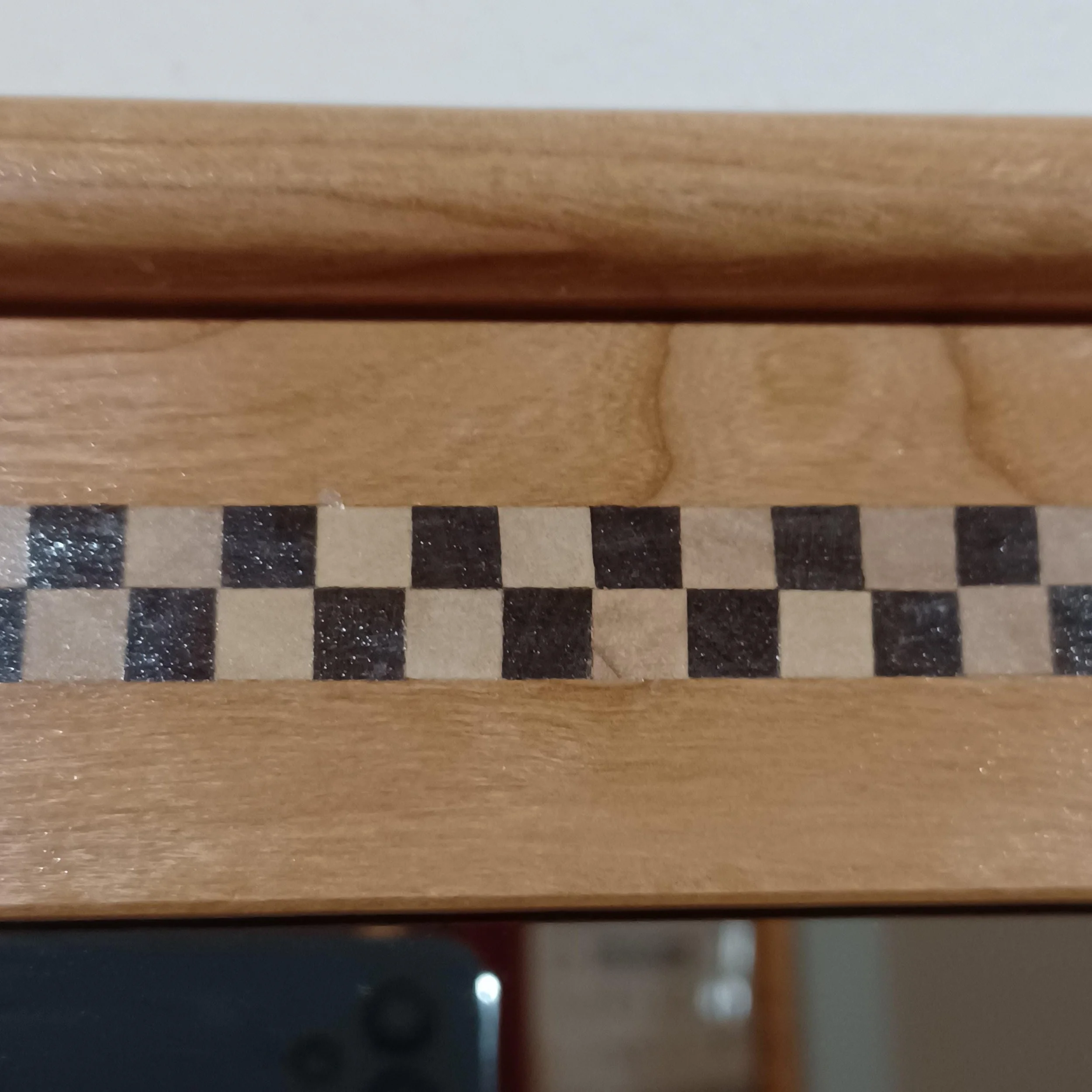 Close-up of a wooden frame with visible grain pattern and a checkered dark and light inlay.