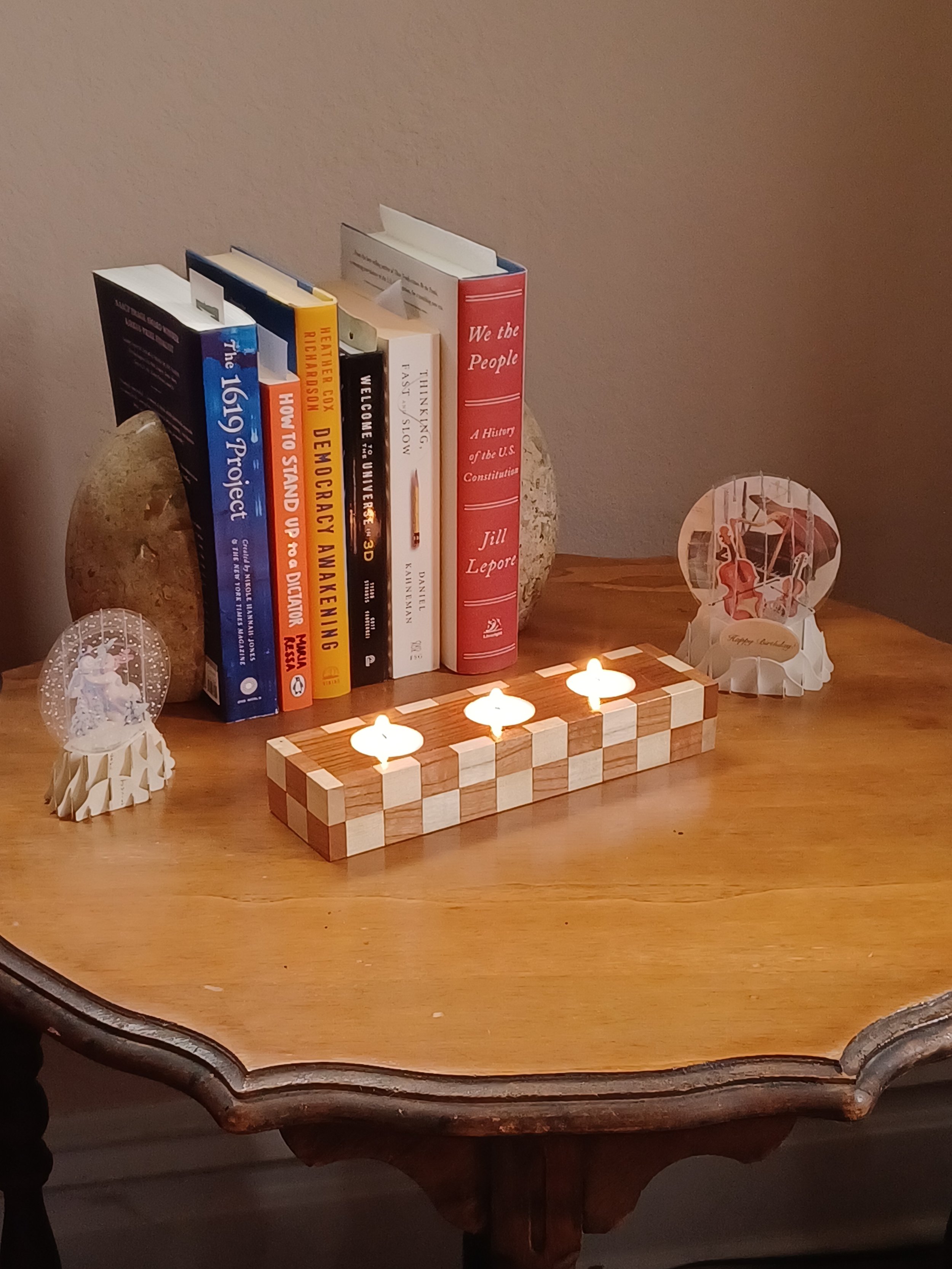 A wooden end table decorated with a tealight candle holder, a row of books standing upright and home decorations nearby.