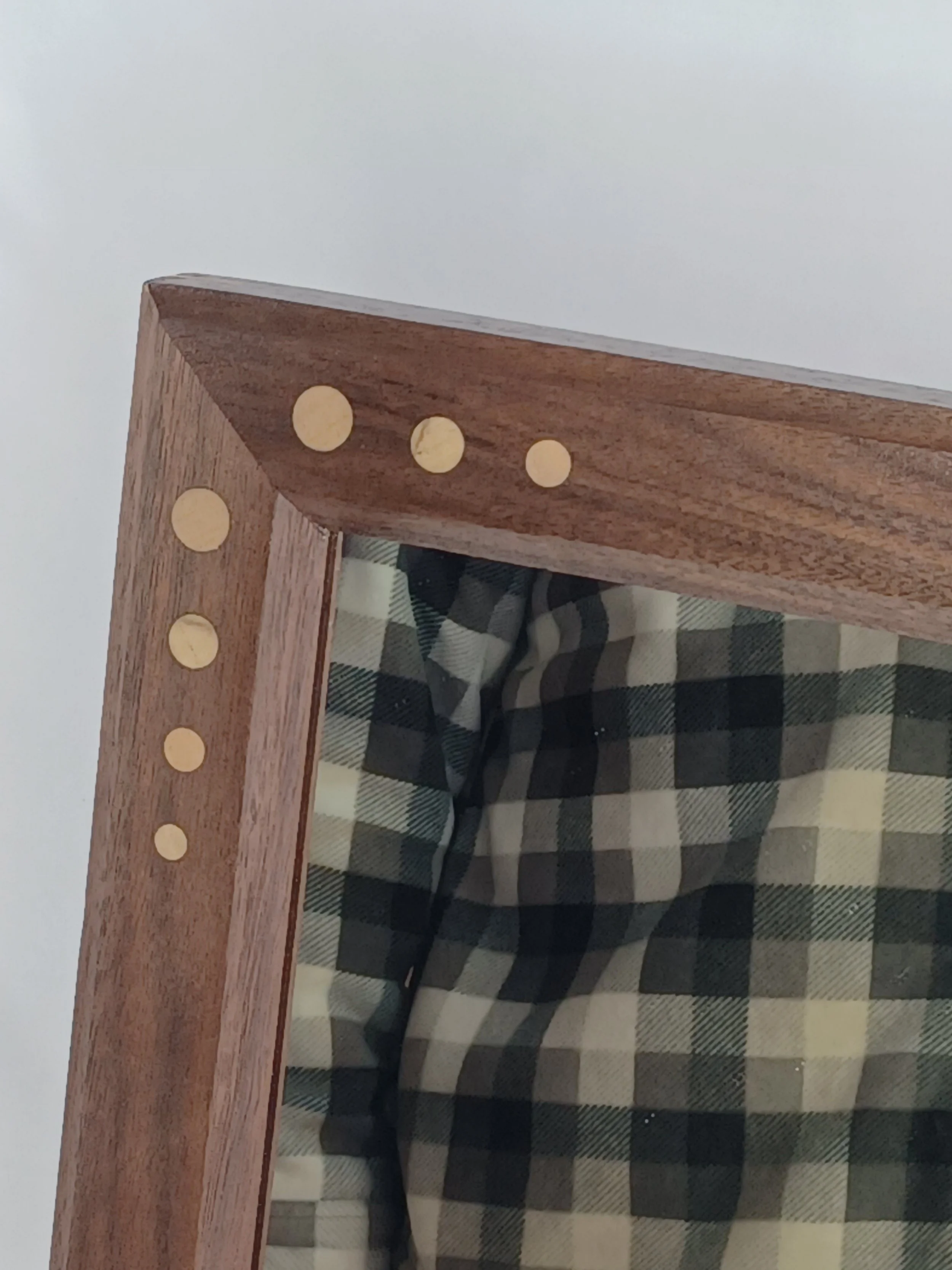 Close-up of a framed mirror, accented with light colored inlayed circles, like polka dots. A checkered fabric is visible in the mirror.