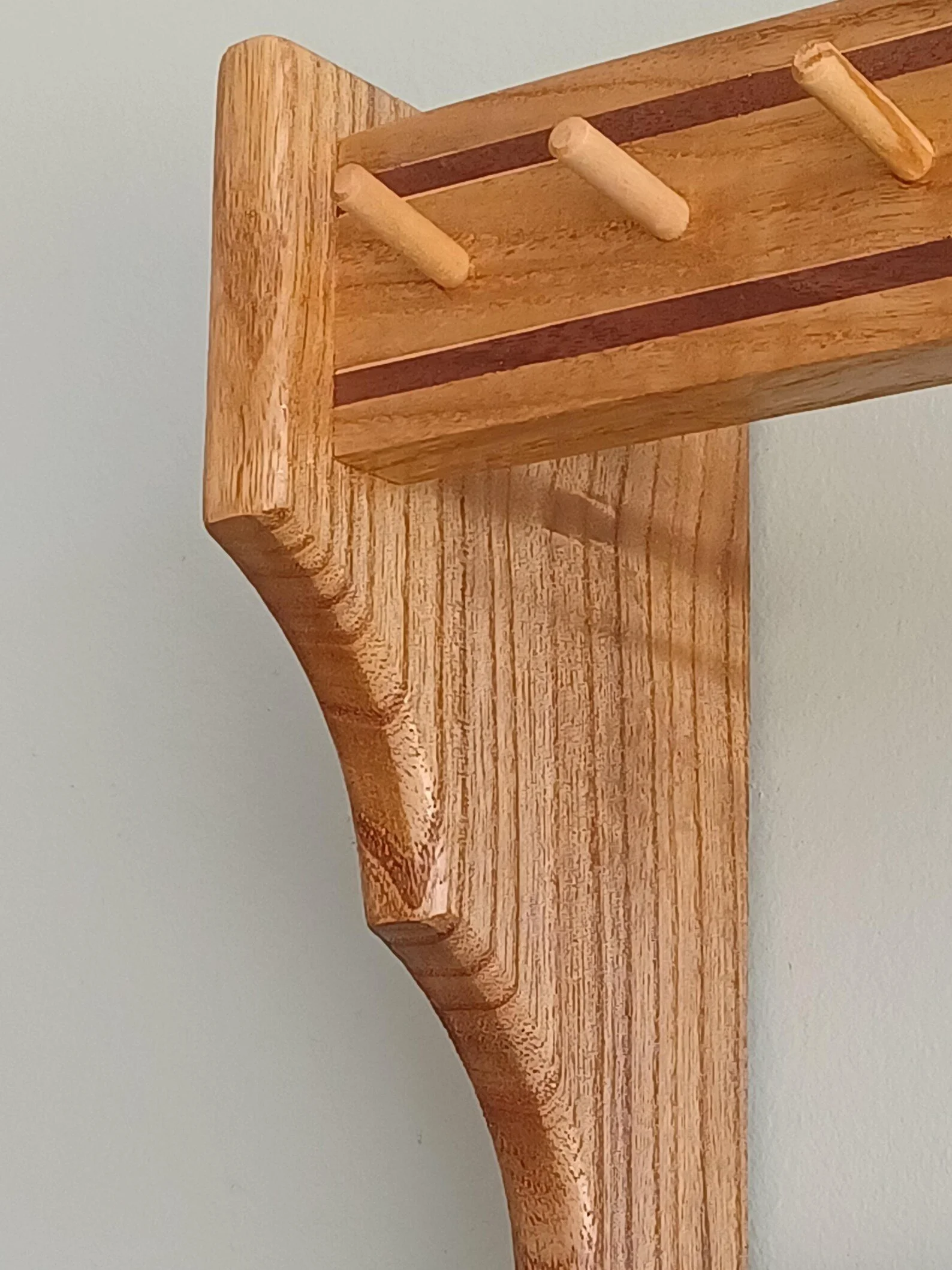 Close-up of a wooden rack with three dowels, finished in natural wood, against a plain light-colored wall.