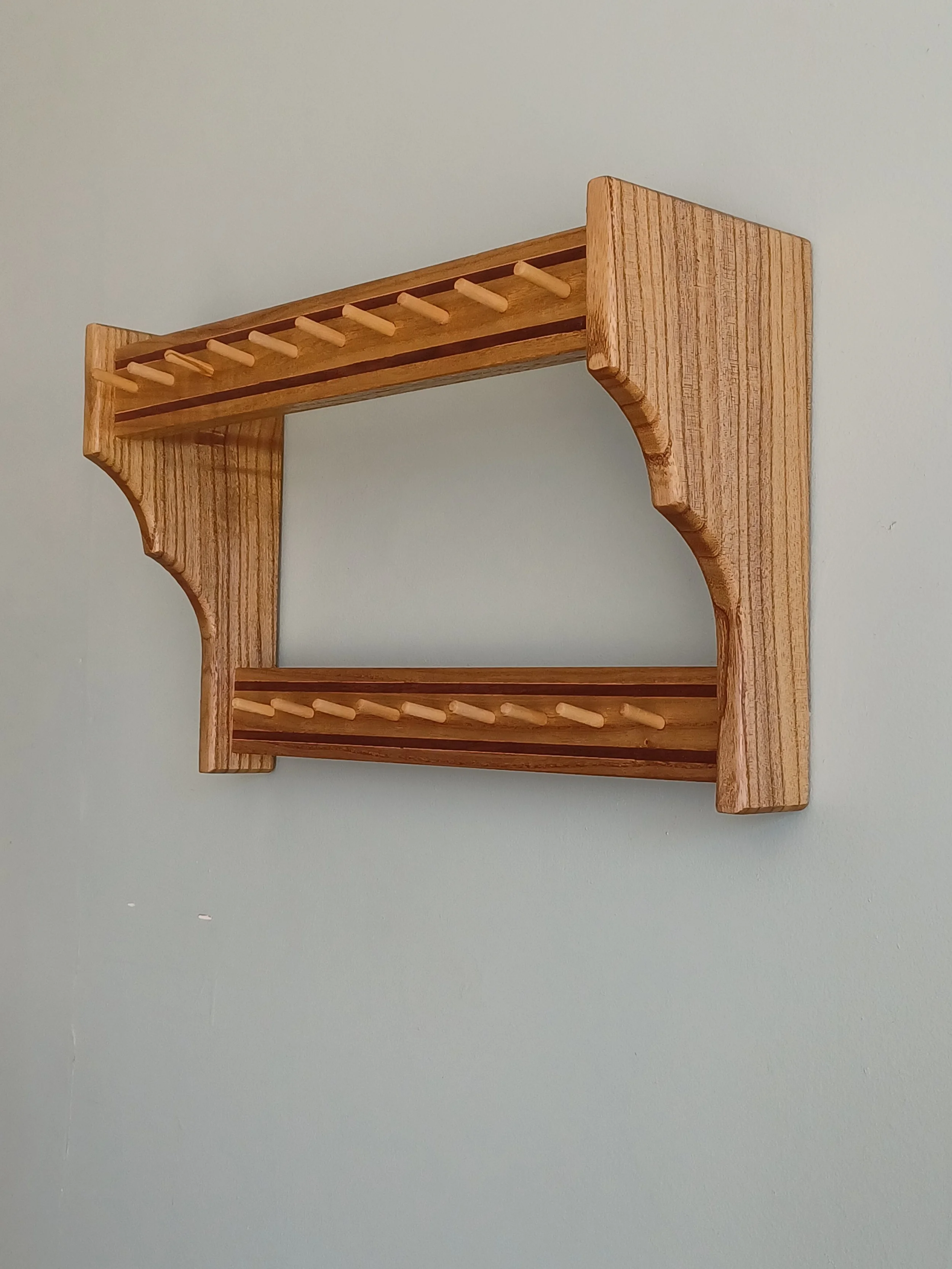 A wooden wall-mounted drying rack with two levels of pegs against a light-colored wall.