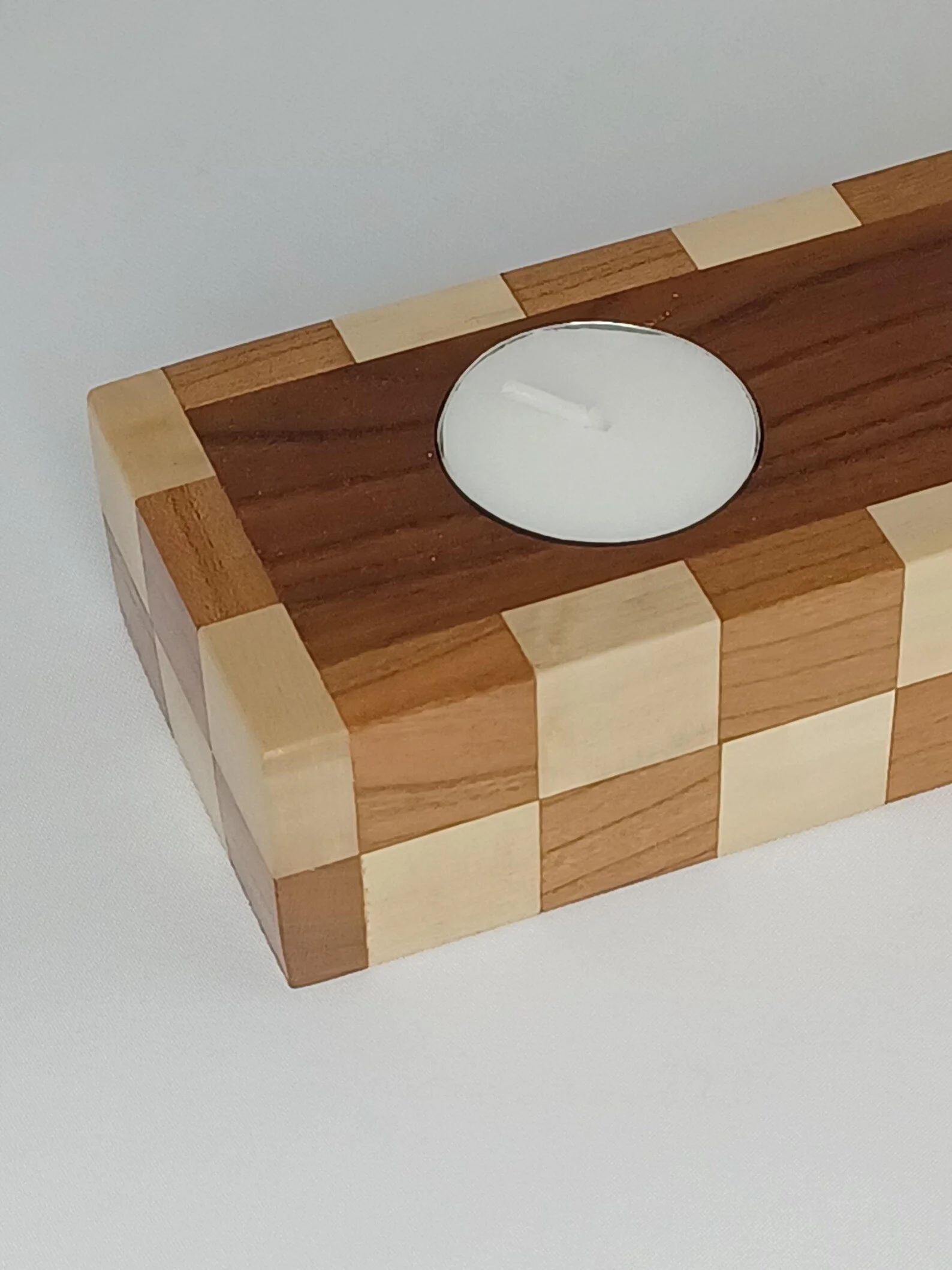A wooden tealight holder with checkerboard patterns and tealight candle inserted on top.