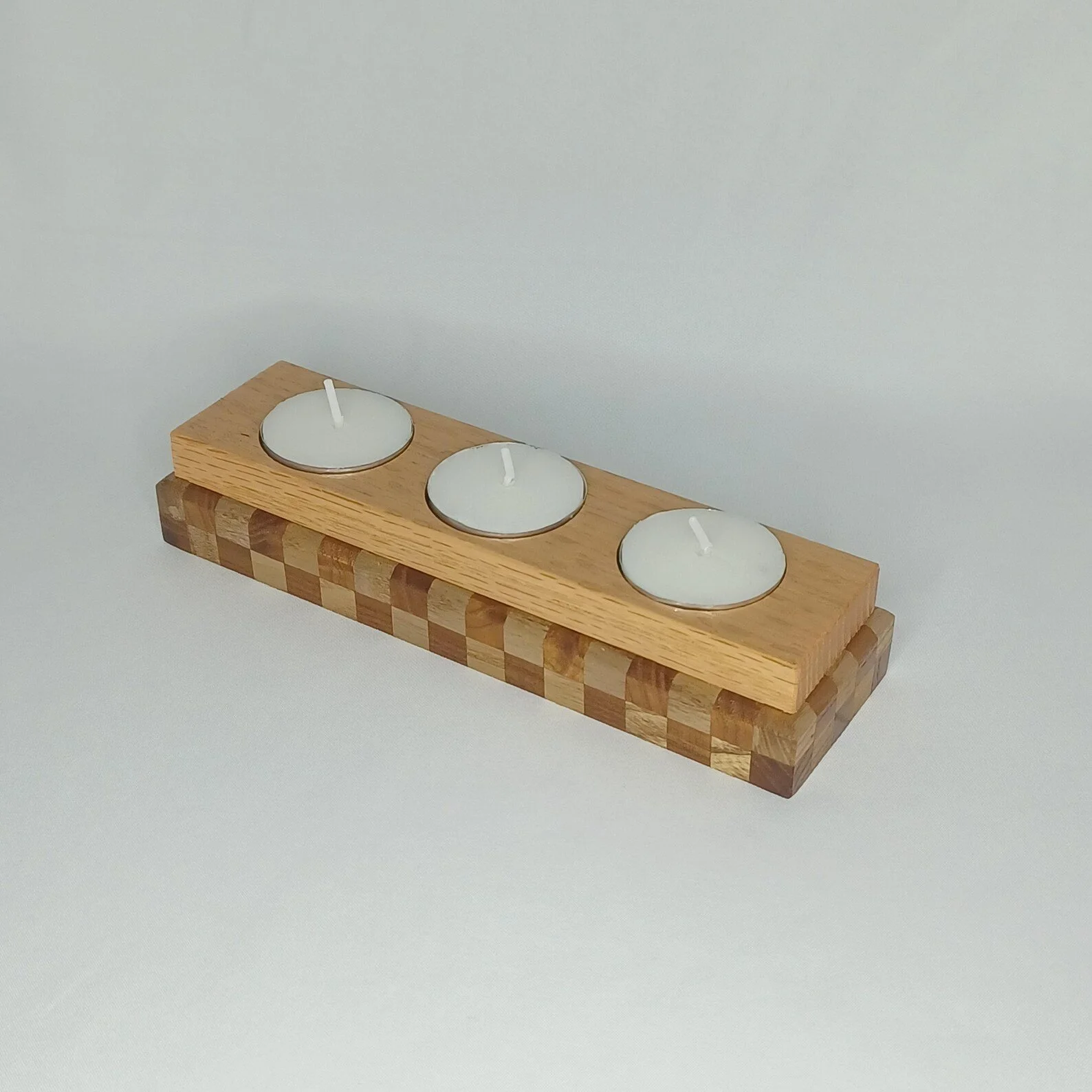 A wooden tealingt holder with three white tealight candles on a plain surface.