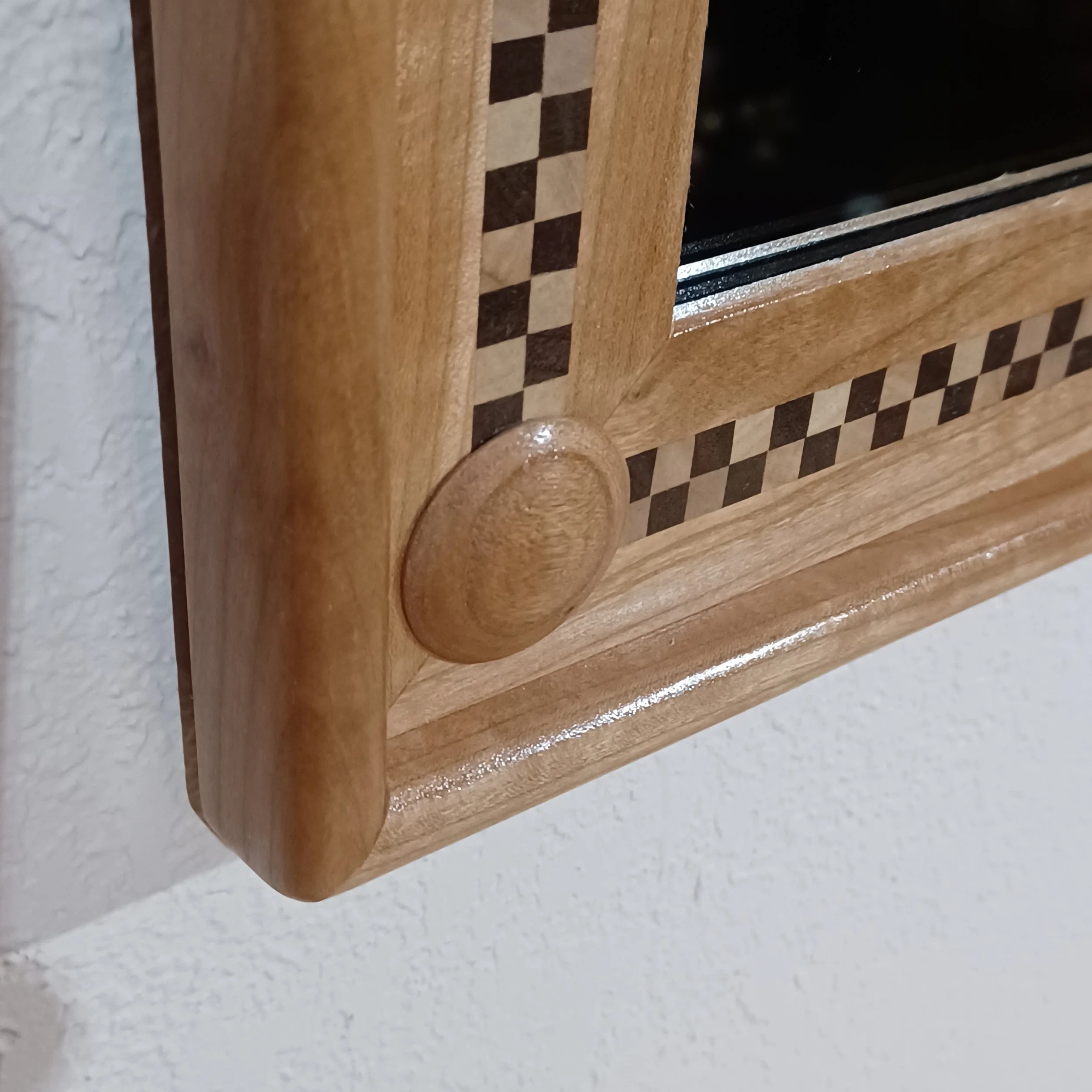 Close-up of the corner of a checkerboard inlaid mirror frame hung on a wall.