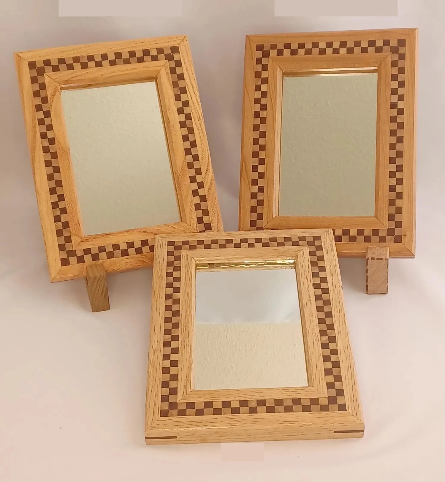 Three wooden picture frames with checkerboard accents, arranged on a white surface, with one leaning against a small wooden block.