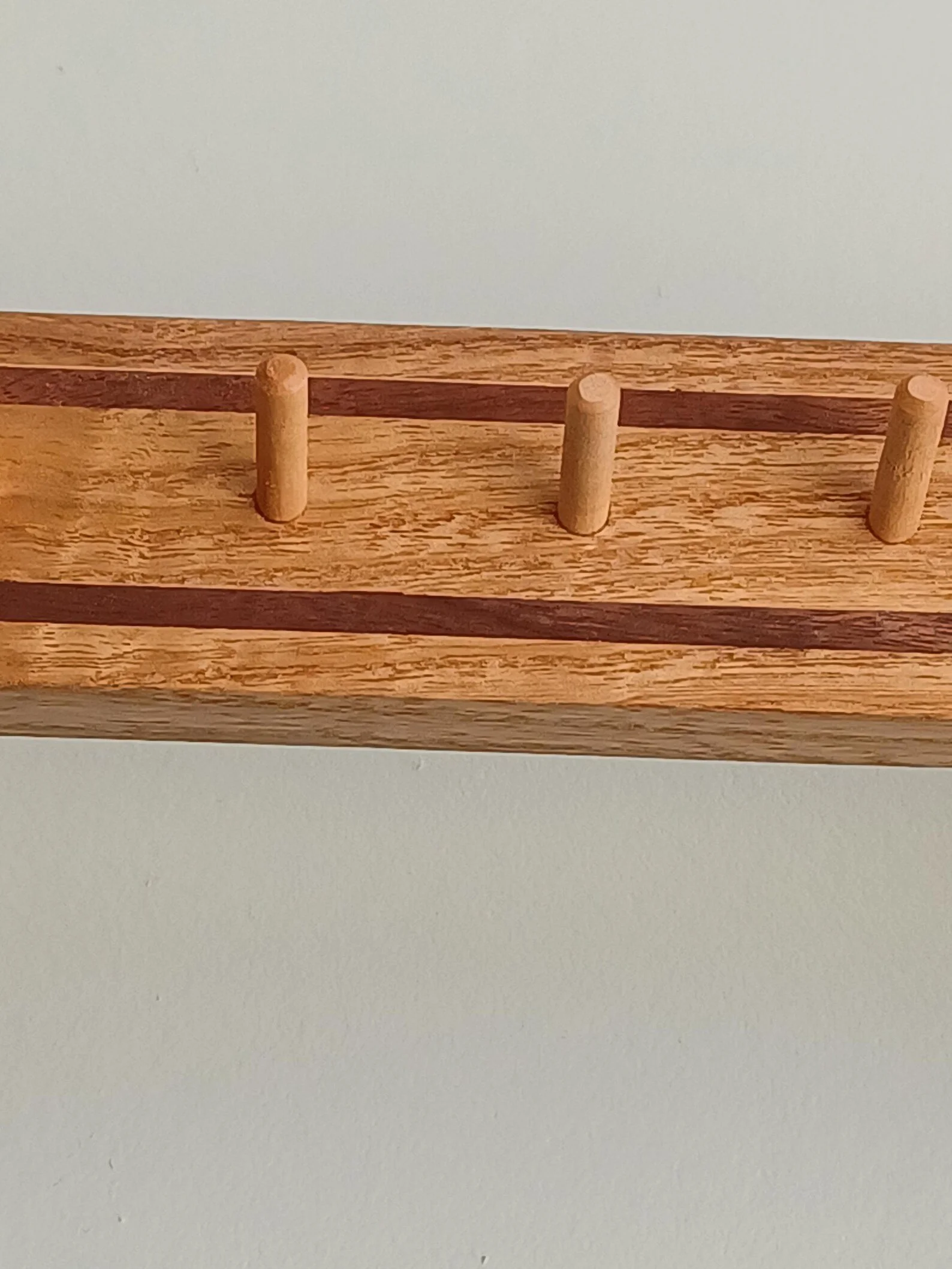 Close-up of a wooden rack with three small cylindrical pegs on a flat surface.