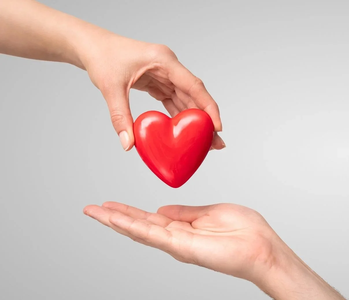 Two hands exchanging a red heart, symbolizing care or love.