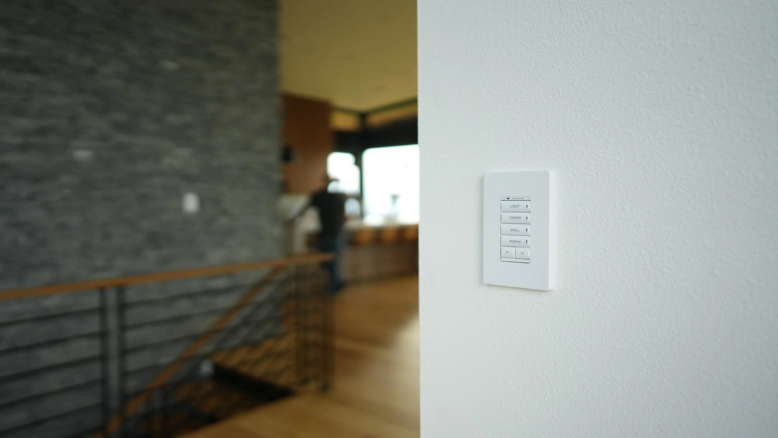 Wall-mounted remote control panel with buttons labeled for lighting, chandelier, wall, porch, and additional controls, in a modern interior space.
