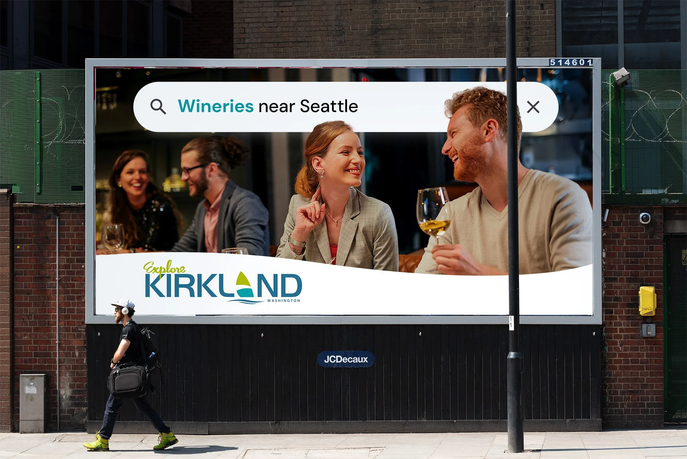 Billboard advertisement featuring people enjoying wine at a restaurant, with a search bar displaying 'Wineries near Seattle' and the phrase 'Explore Kirkland, Washington'.