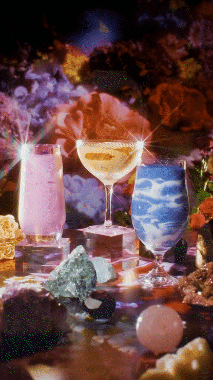 Three colorful cocktails in glasses on a table with decorative rocks and gems, with a nebulous, cosmic background.