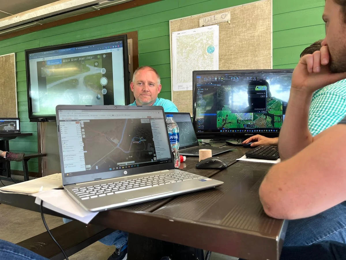 Keith Conville sitting at a desk with computer monitors showing GIS displays.