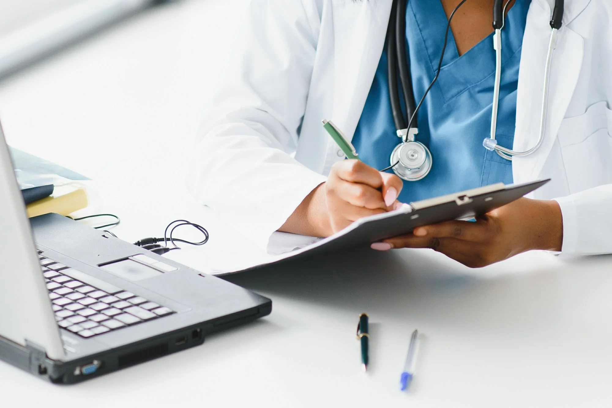 Doctor sitting at the computer writing on a clipboard