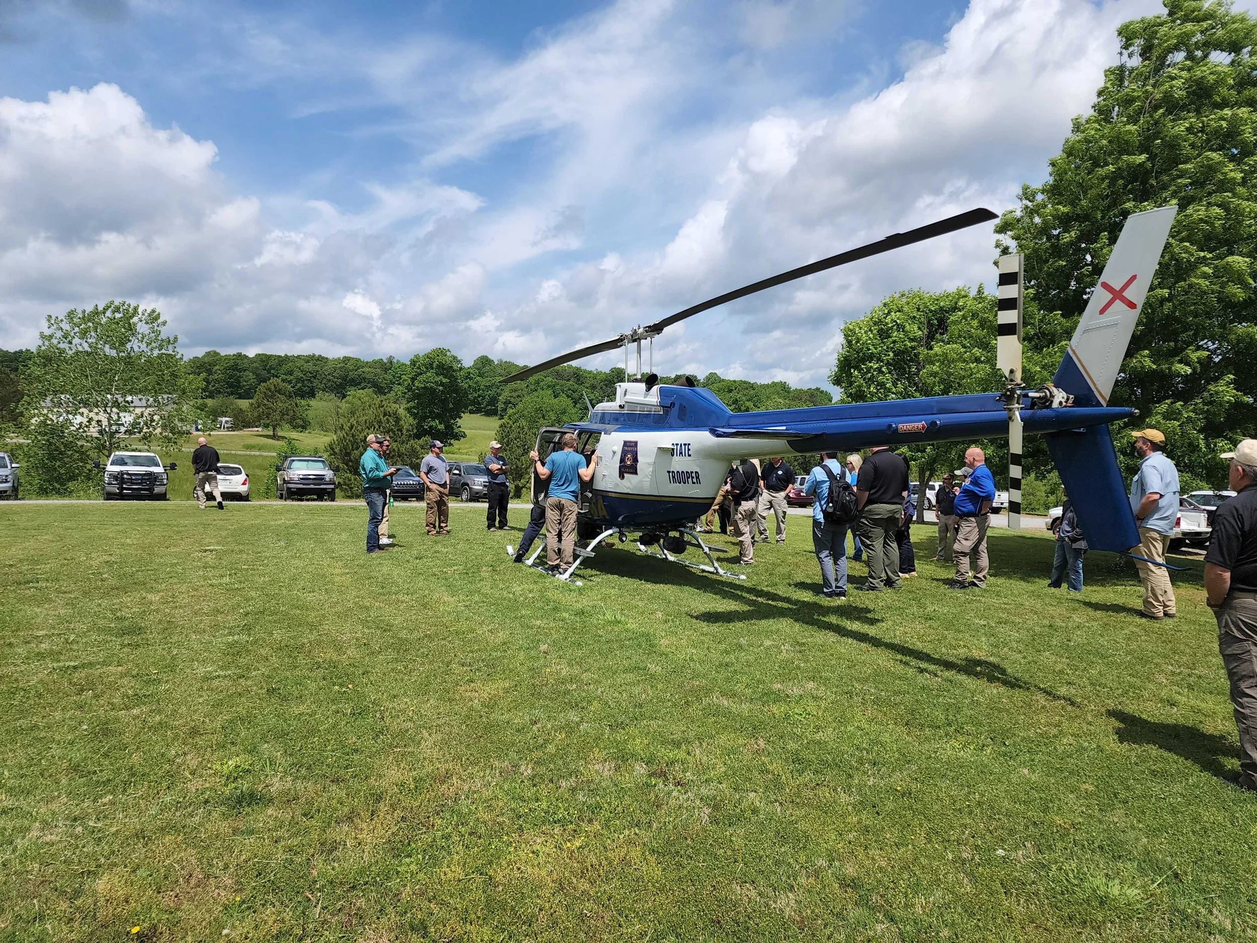 Stationary State Trooper helicopter in a field  surrounded by people.