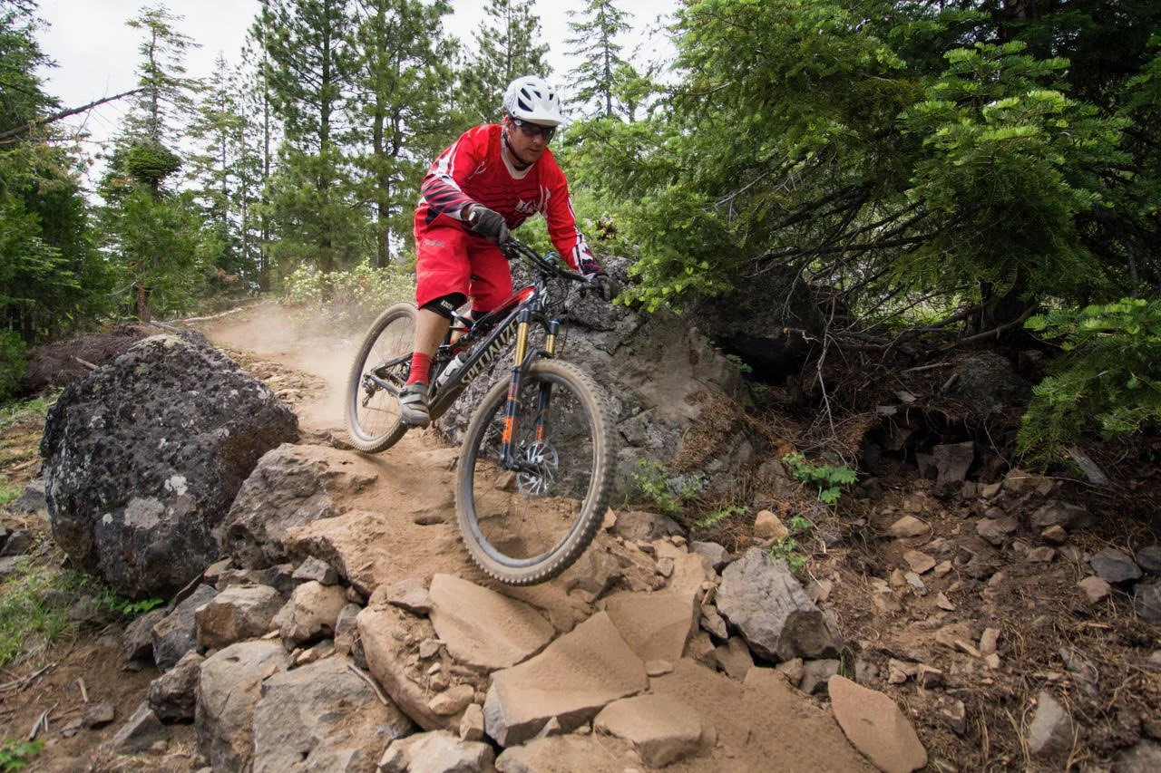 A mountain biker comes around a corner on a rocky path through the forest.