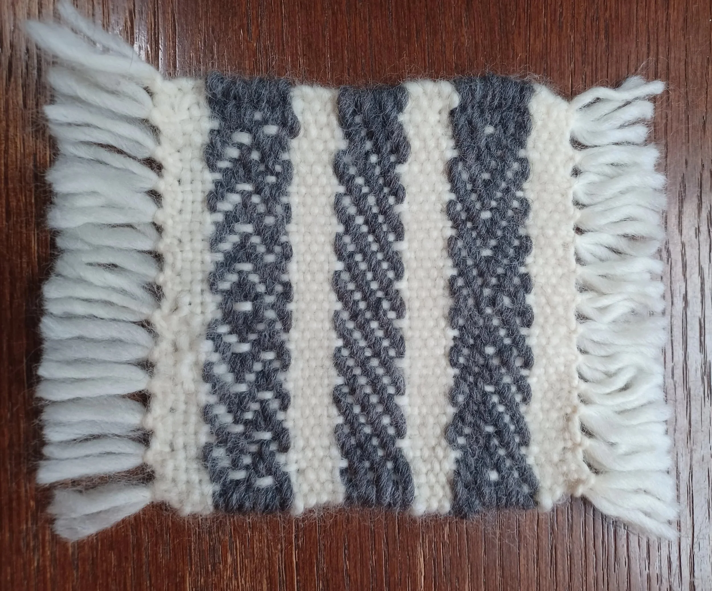 A small woven rug with black and white twill pattern on a wooden floor.
