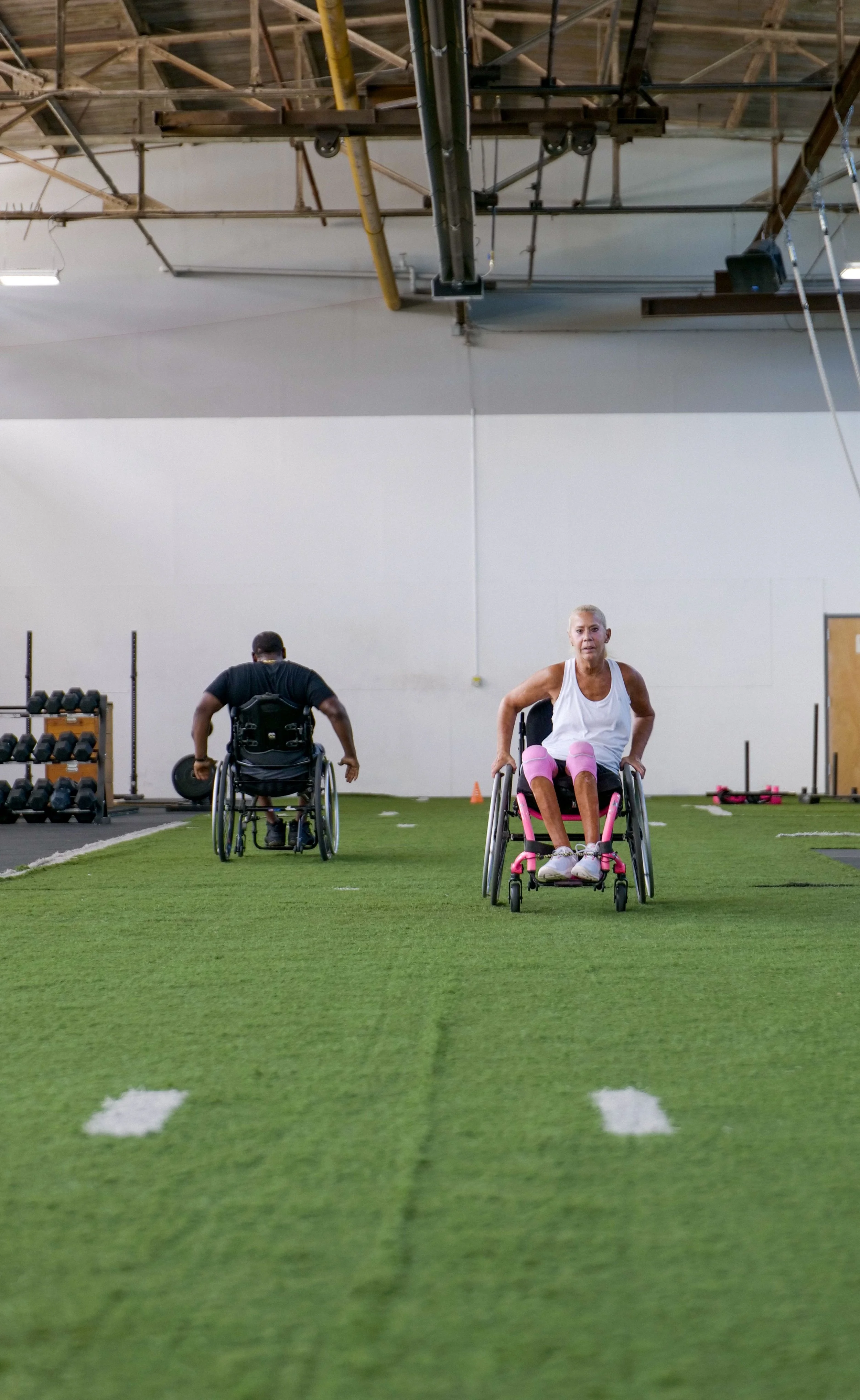 Two athletes in wheelchairs racing indoors on a track.