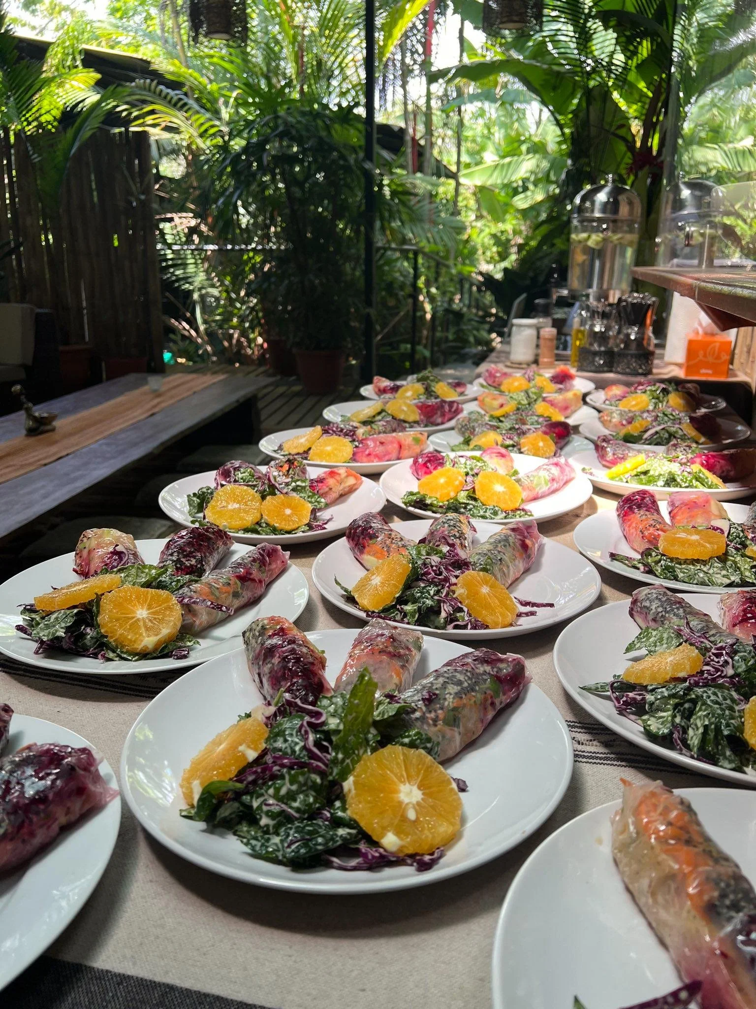 Plates with spring rolls and orange slices on a table in a tropical setting.